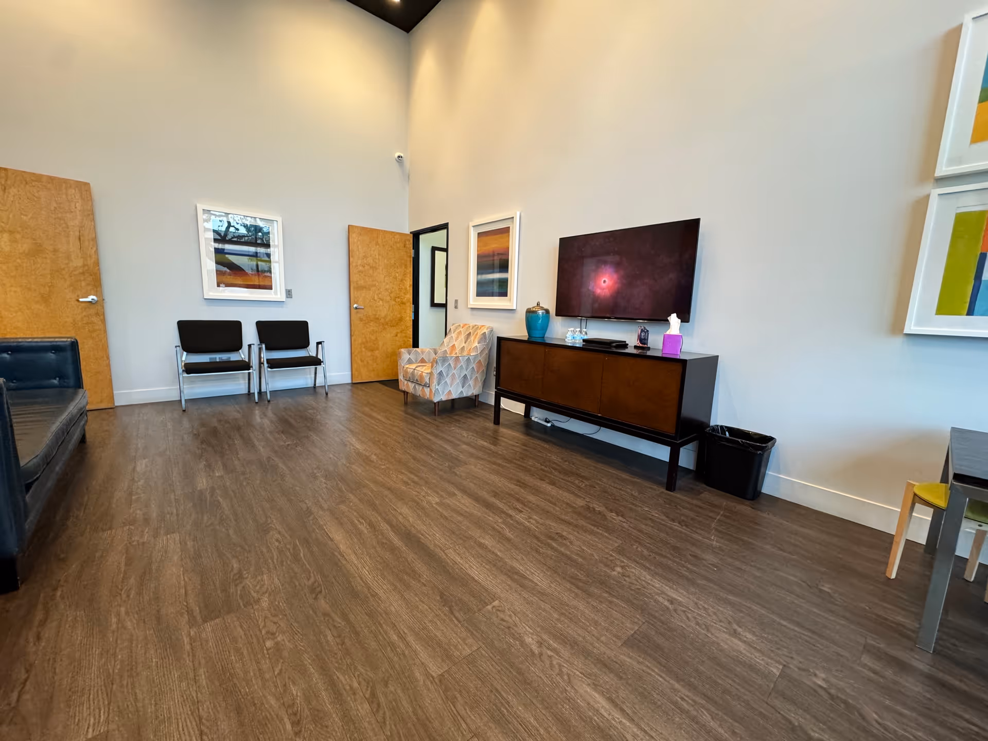 Modern senior living lounge with TV, chairs, a sofa, and wooden floor.