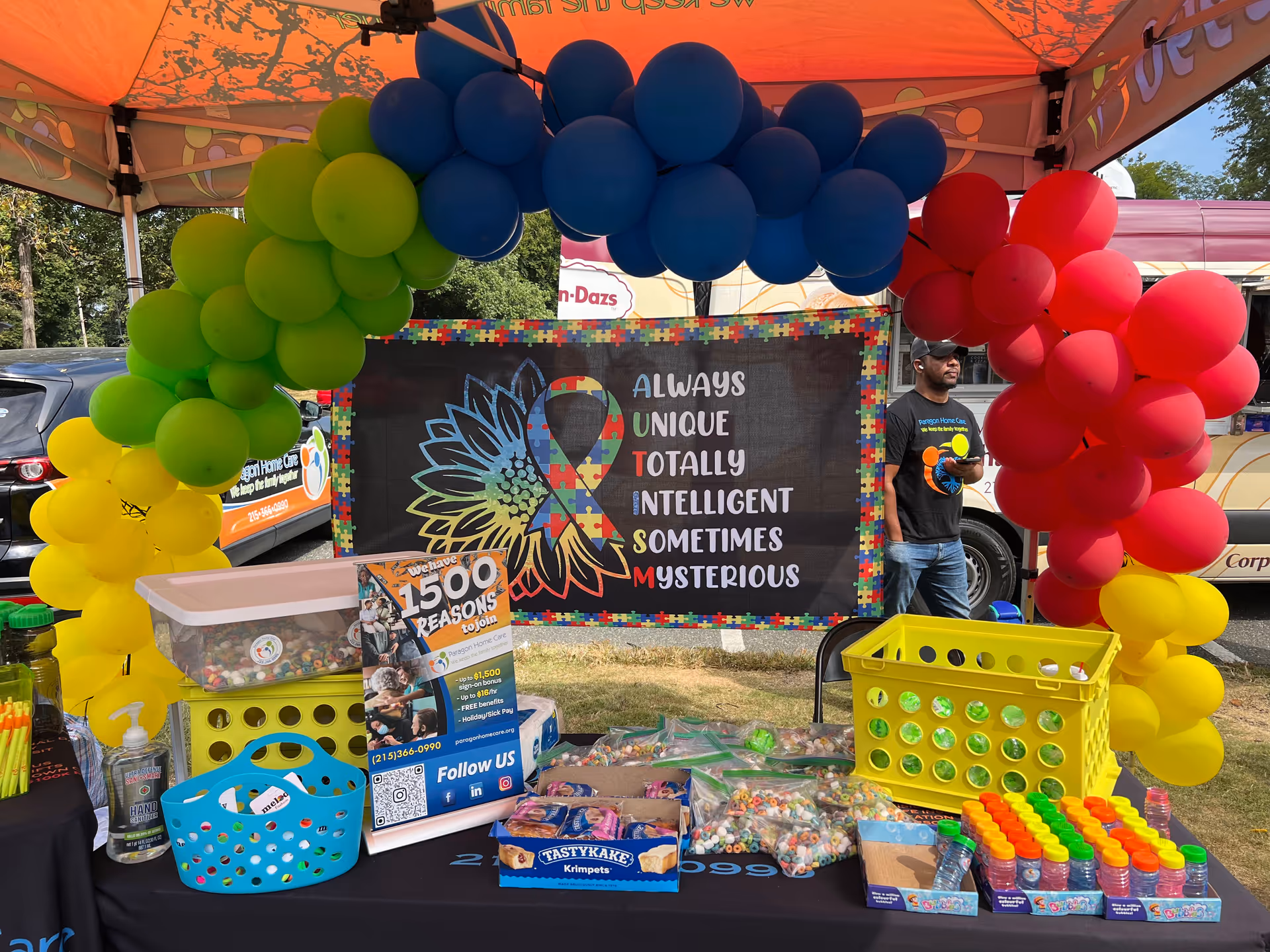 Outdoor booth for Paragon Home Care under a balloon arch, with banner and goodies.