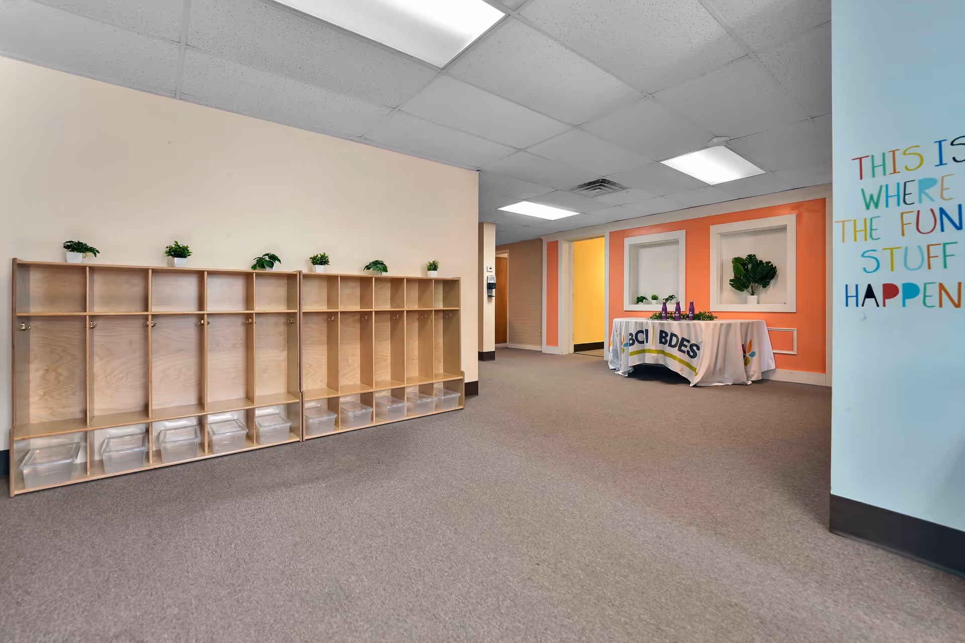 Empty interior featuring wooden cubbies, bright wall accents, and a welcoming table.