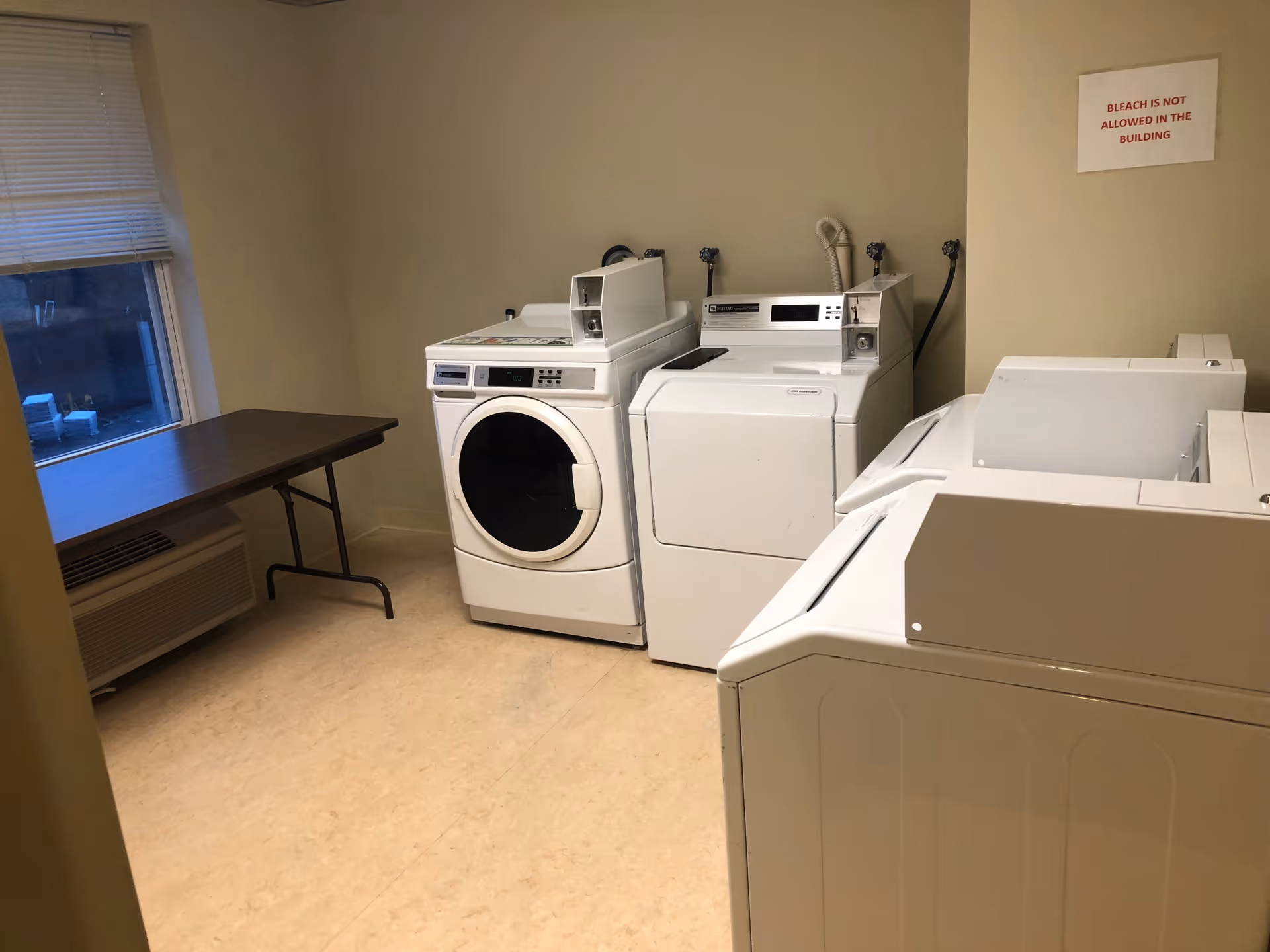 Laundry room with front-loading washer and dryer, folding table, window, and wall sign.