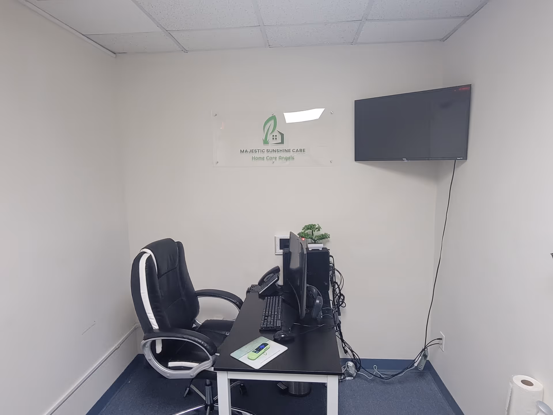 Small office with desk, computer, sign reading Majestic Sunshine Care, and wall-mounted TV.