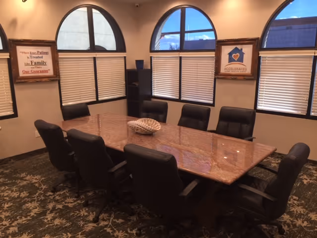 Conference room with a large wooden table, black chairs, and arched windows with blinds.