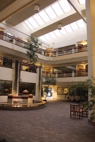Multi-level interior atrium with skylights, potted trees, benches, and a circular fountain.