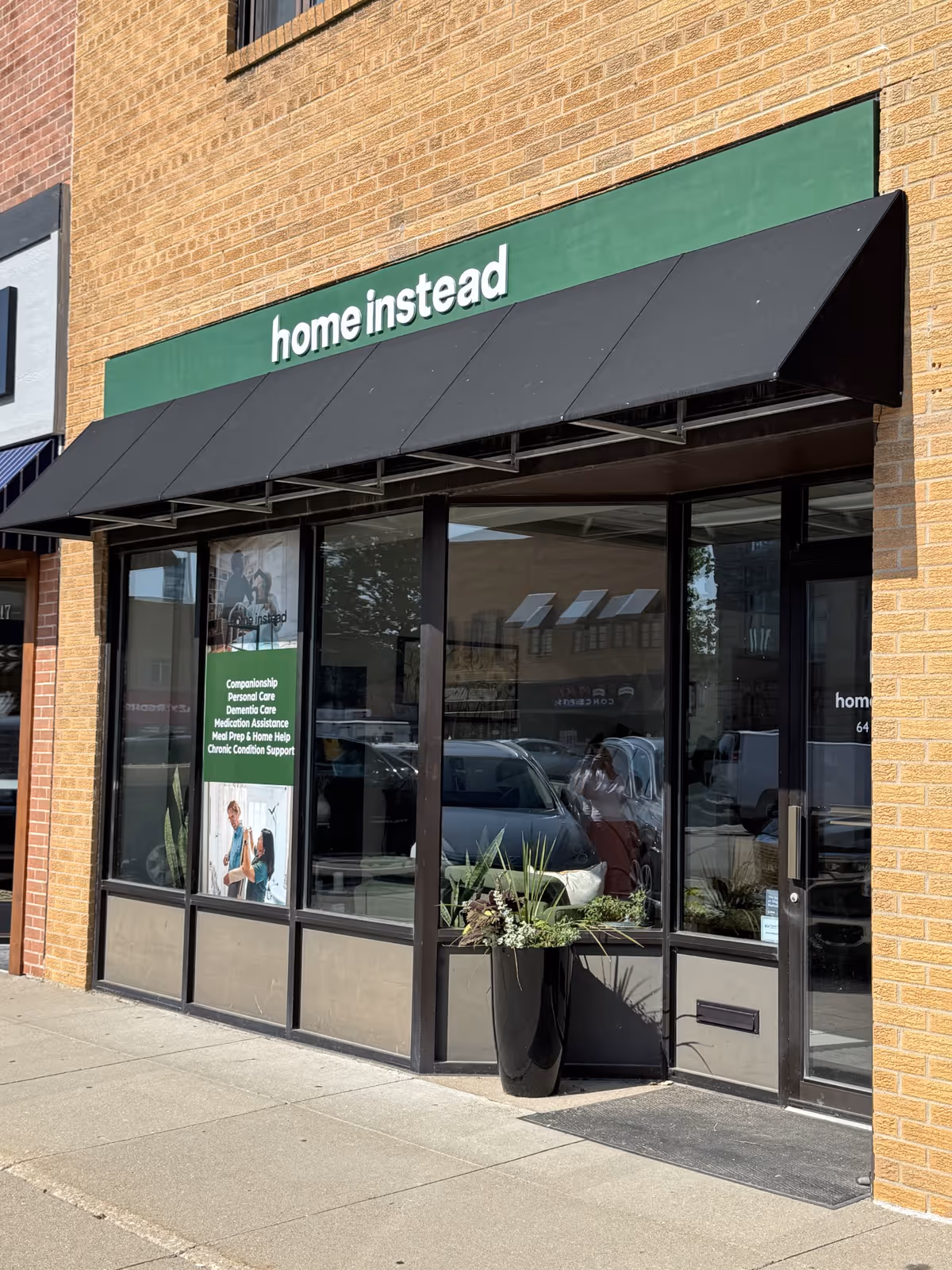 Exterior of a Home Instead storefront with large windows and a black awning.