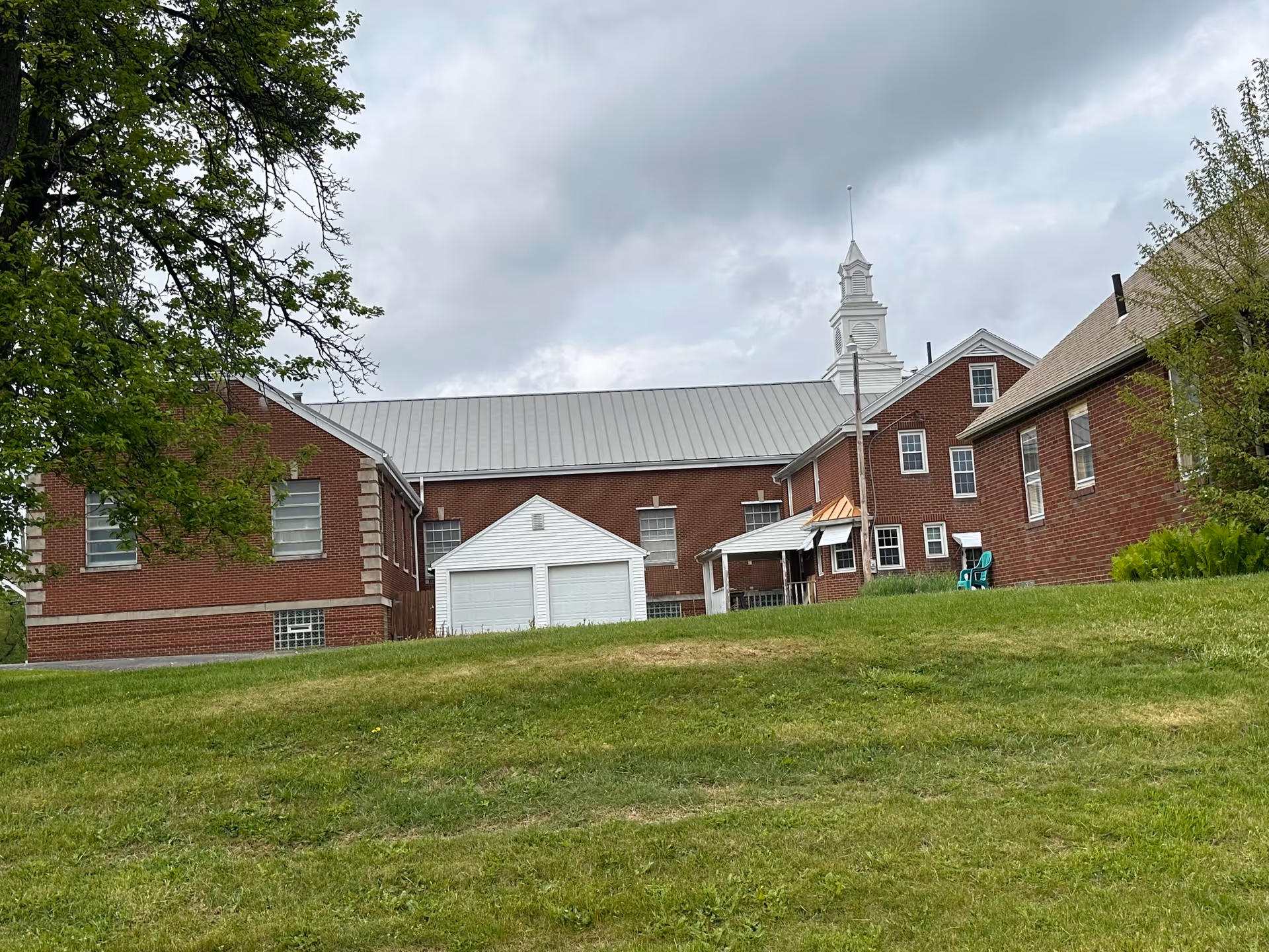 Brick senior living facility exterior with a white shed, green lawn, and trees.