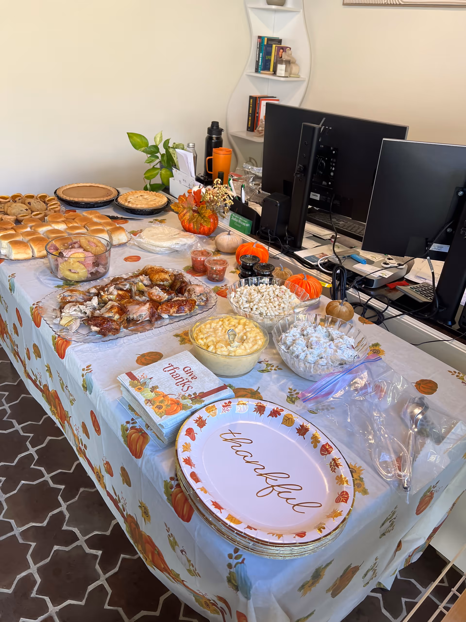 Indoor office space with a long fall-themed buffet table of assorted foods.