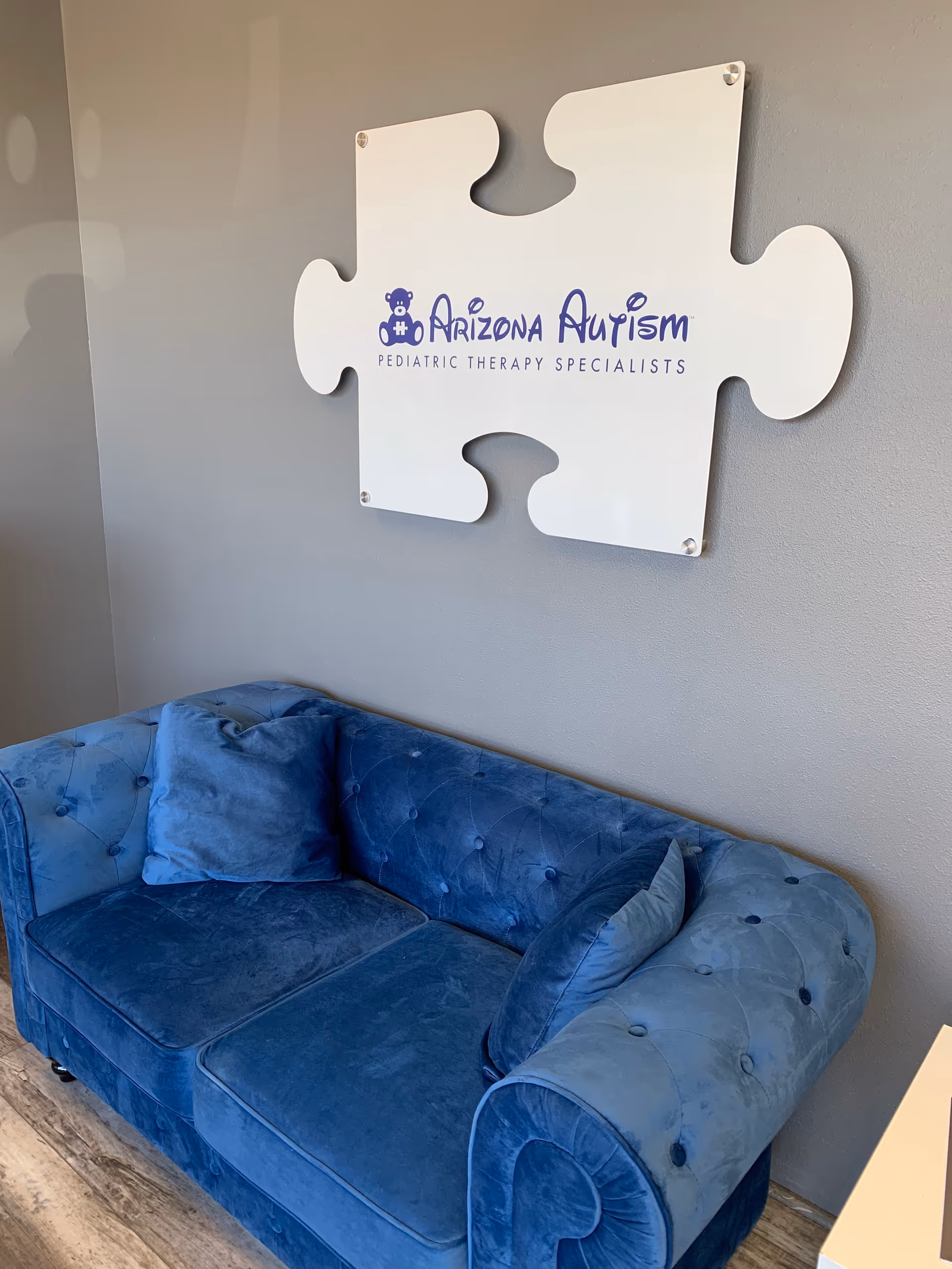 Blue tufted couch sits in a waiting area beneath a puzzle-piece sign.