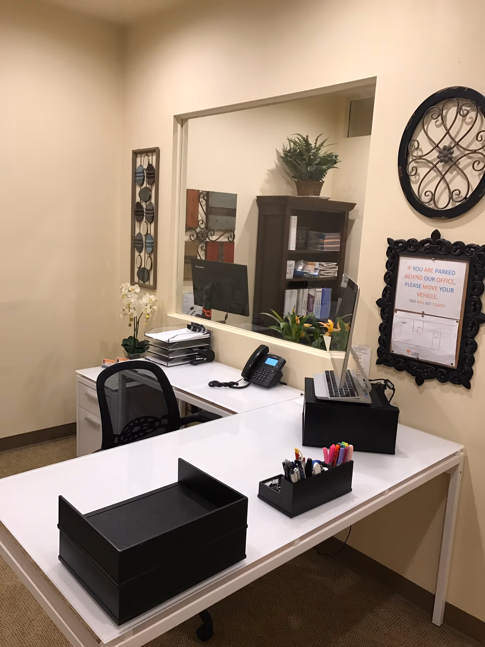A clean office desk area in a reception space with computer, organizers, and decorative wall art.