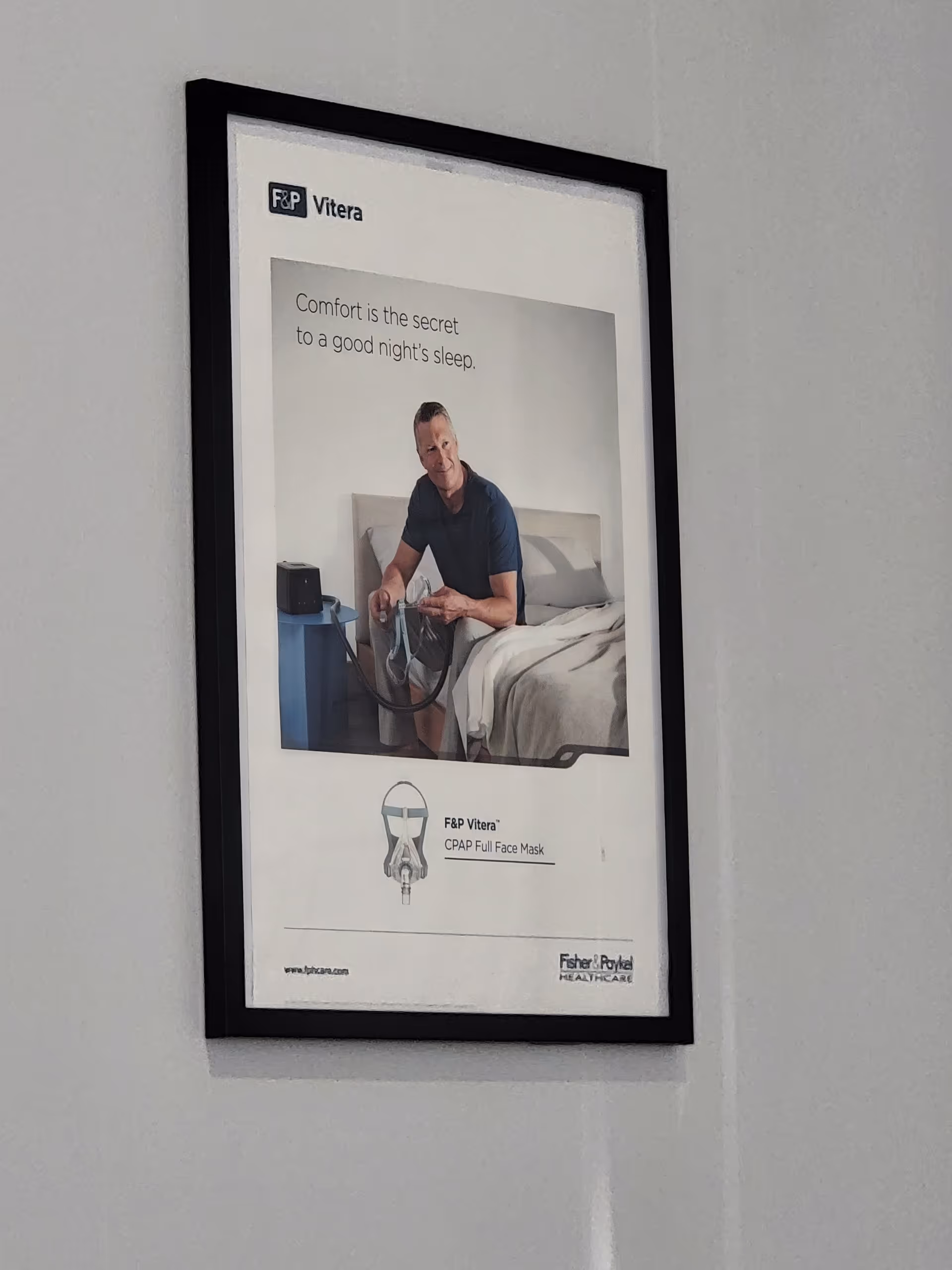 Framed poster advertising CPAP mask on a wall in an interior facility hallway