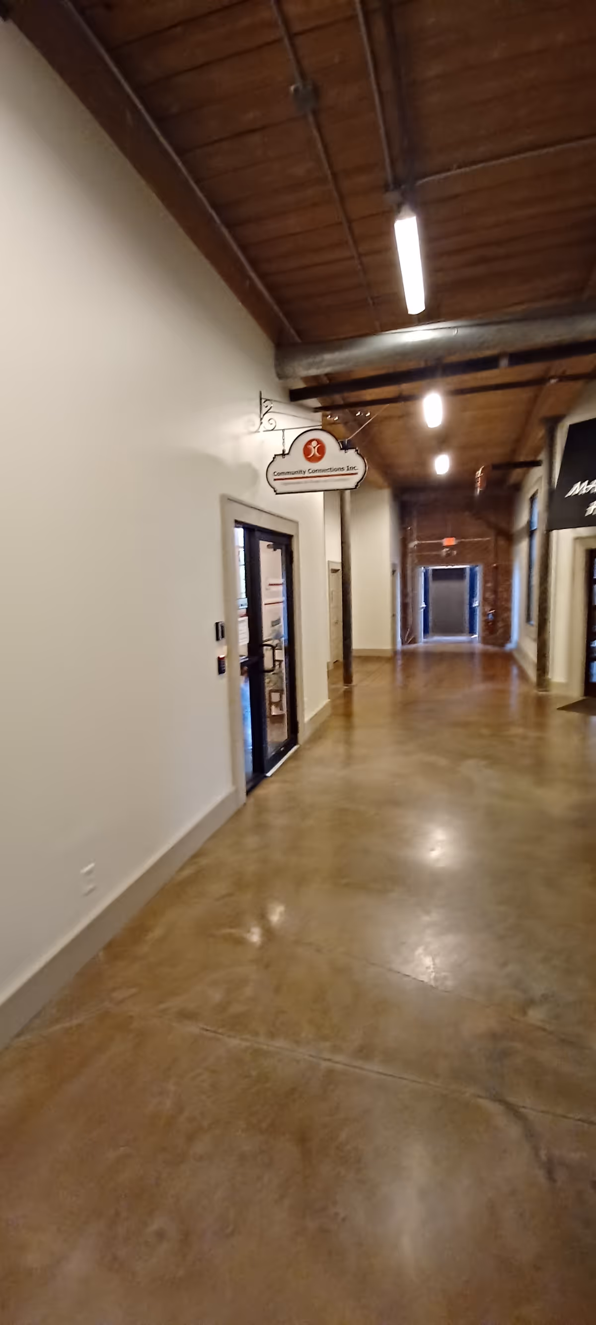 Long, well-lit corridor inside a facility featuring exposed wooden ceiling beams and glass doors.