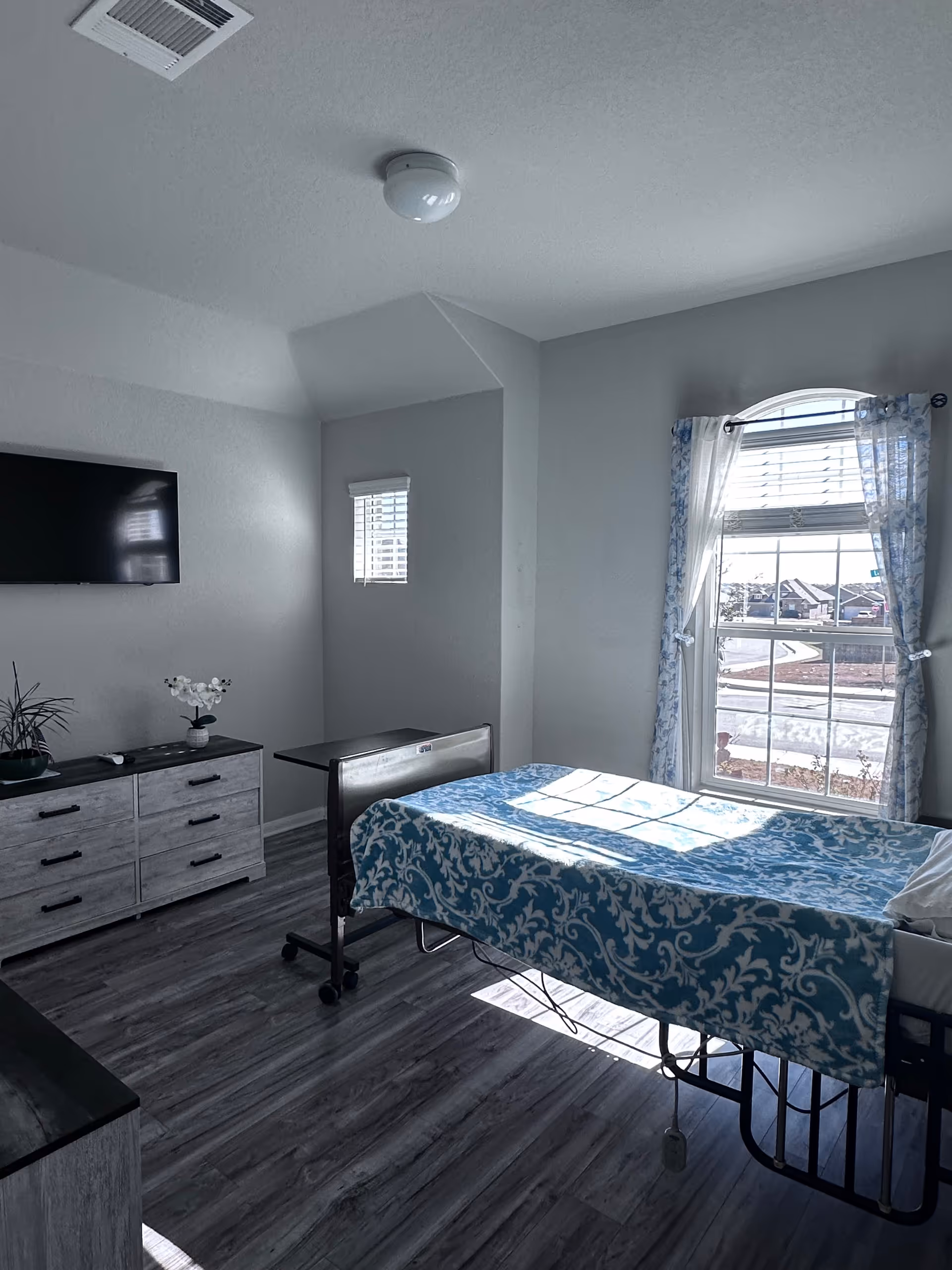 Bright bedroom in Angels of Hope Care Home with a patterned bed, dresser, and large window
