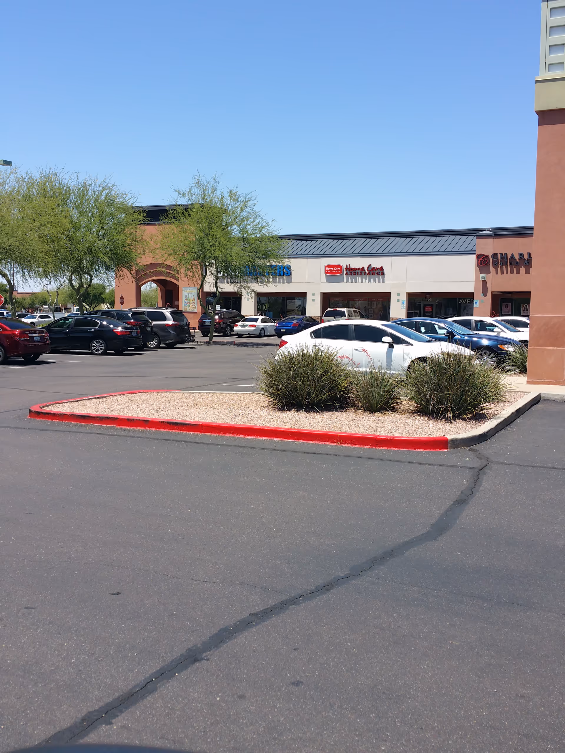 Exterior view of a strip mall with parked cars and storefronts under a blue sky.