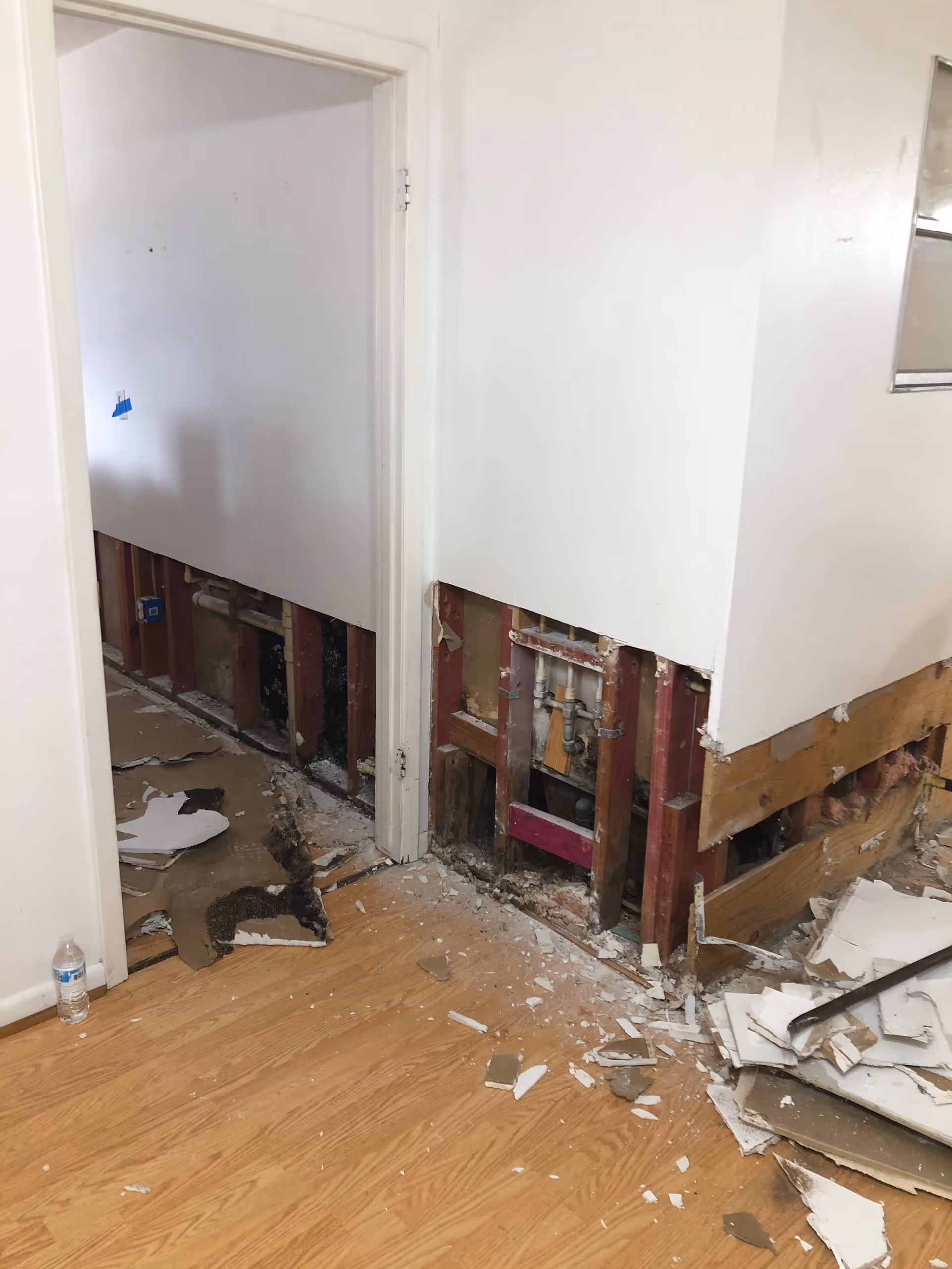 Interior of a senior facility with a partially demolished wall, exposed studs, and debris.