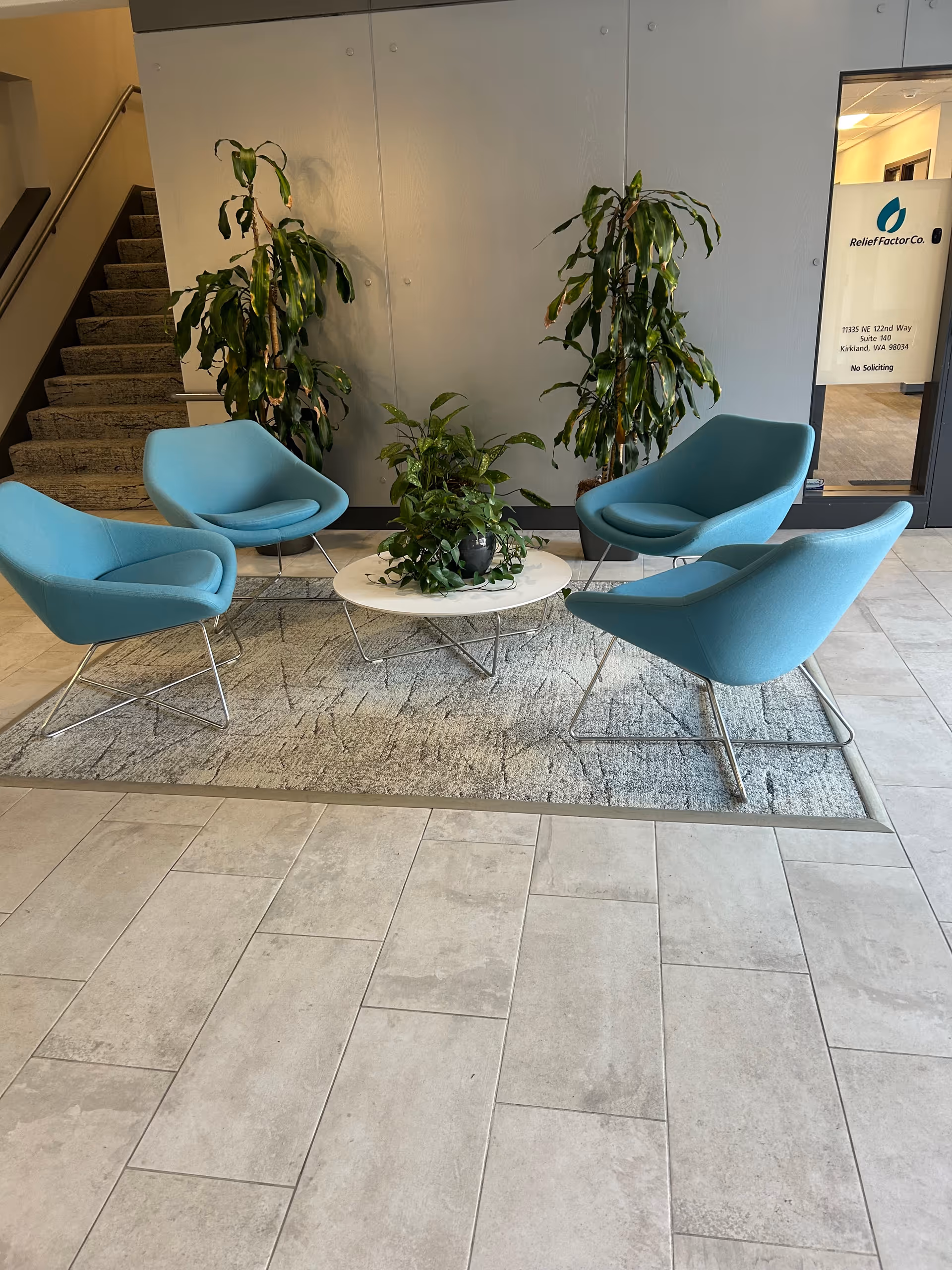 Modern lobby seating area with four turquoise chairs around a white coffee table and plants