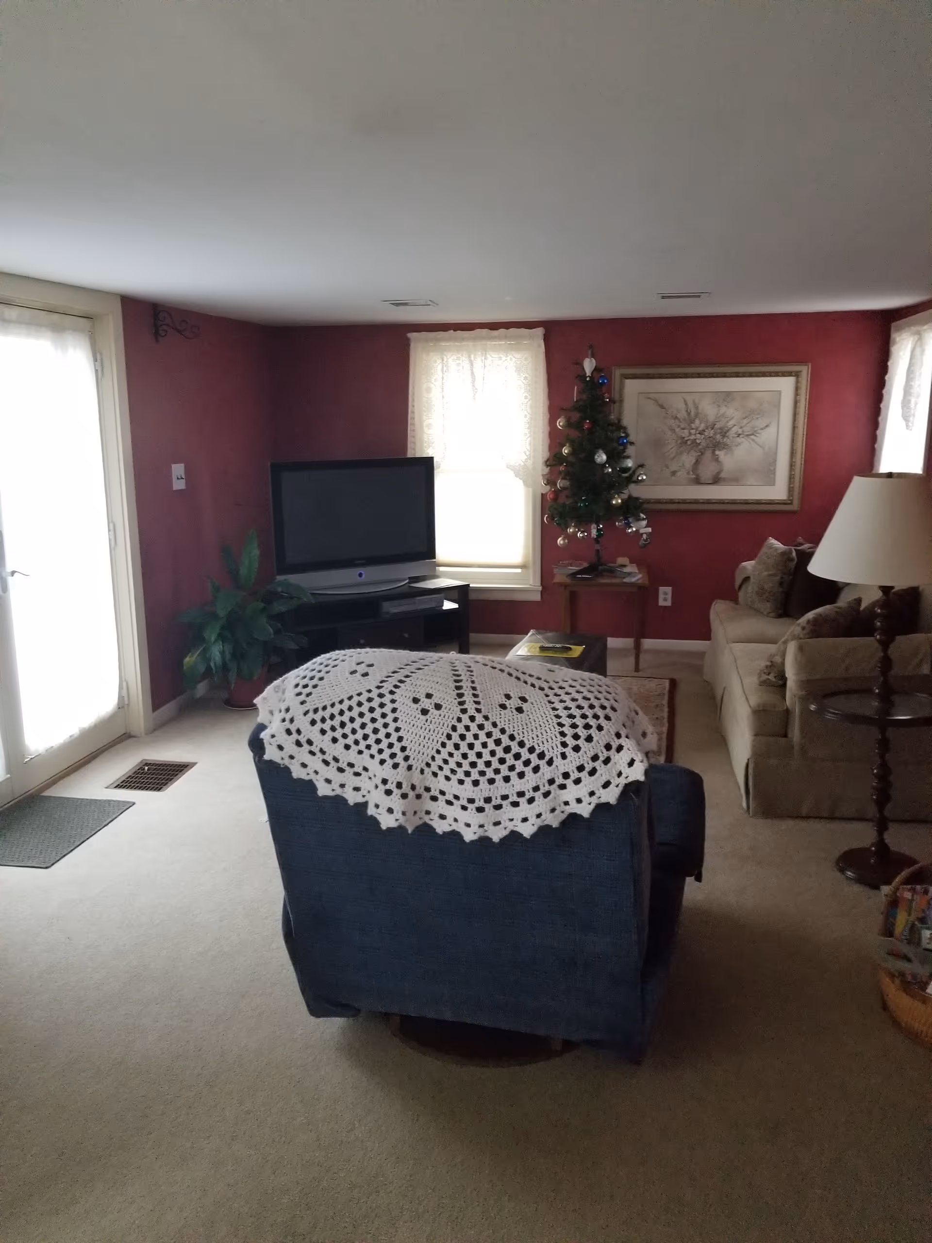 Cozy living room with red walls, Christmas tree, TV, sofa, and crocheted blanket.