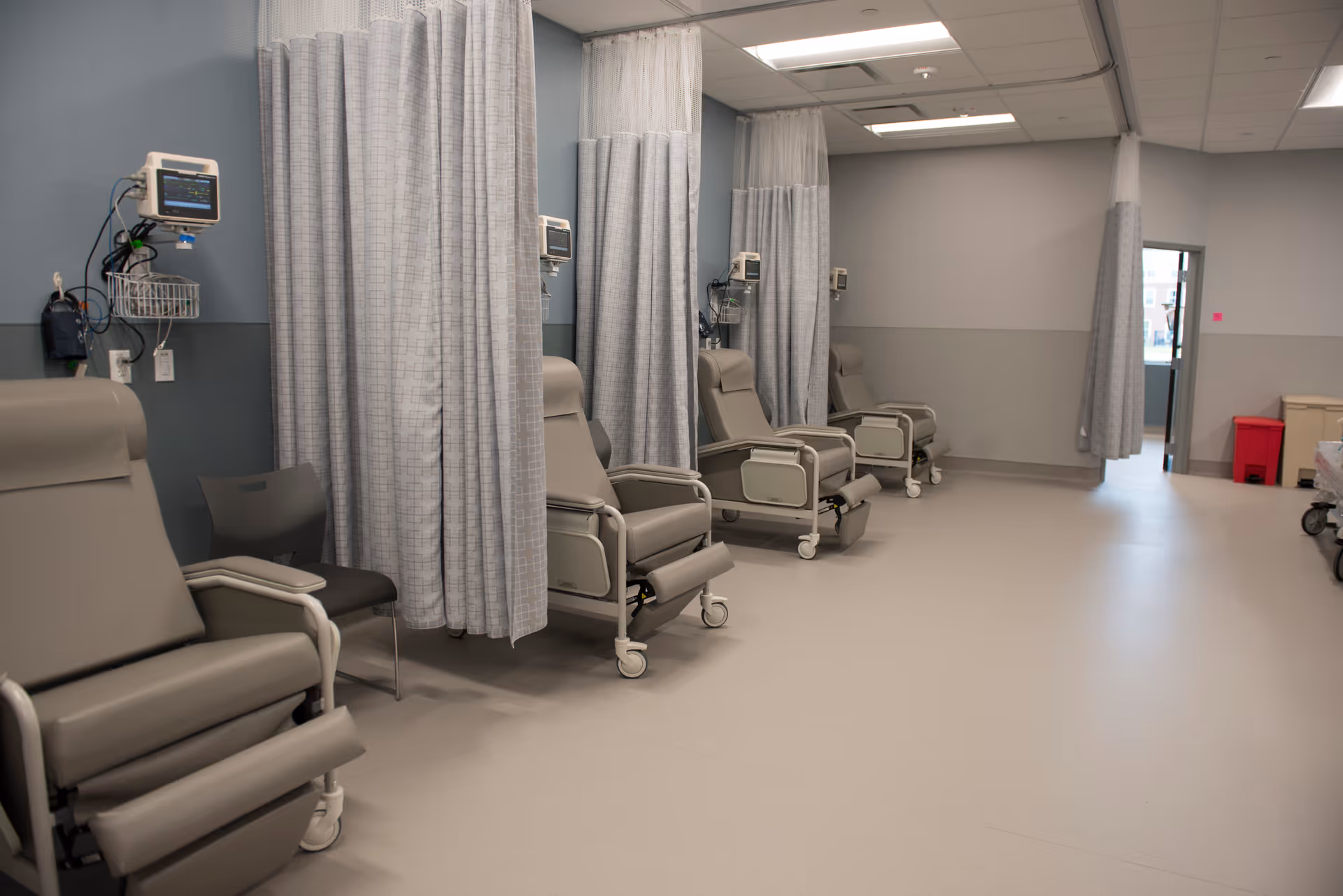 Row of medical chairs with privacy curtains in a clinical infusion area.