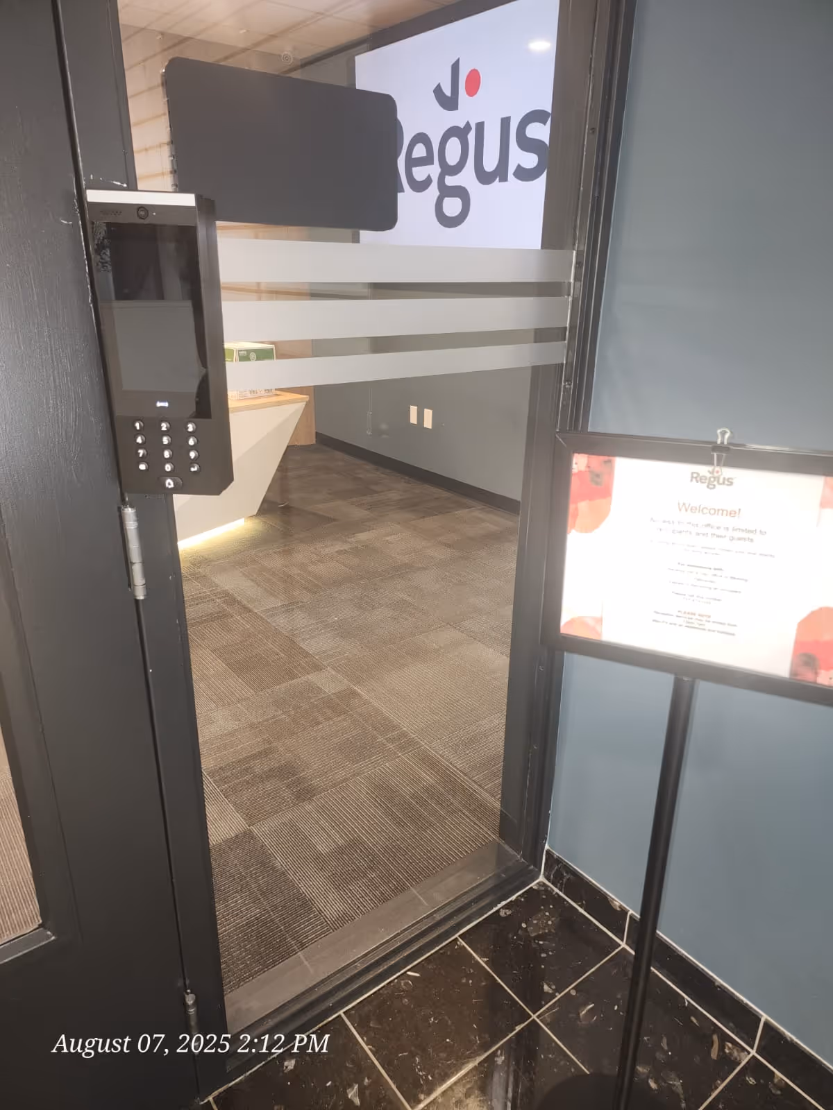 Interior entry lobby with keypad access, glass walls, and a welcome sign.