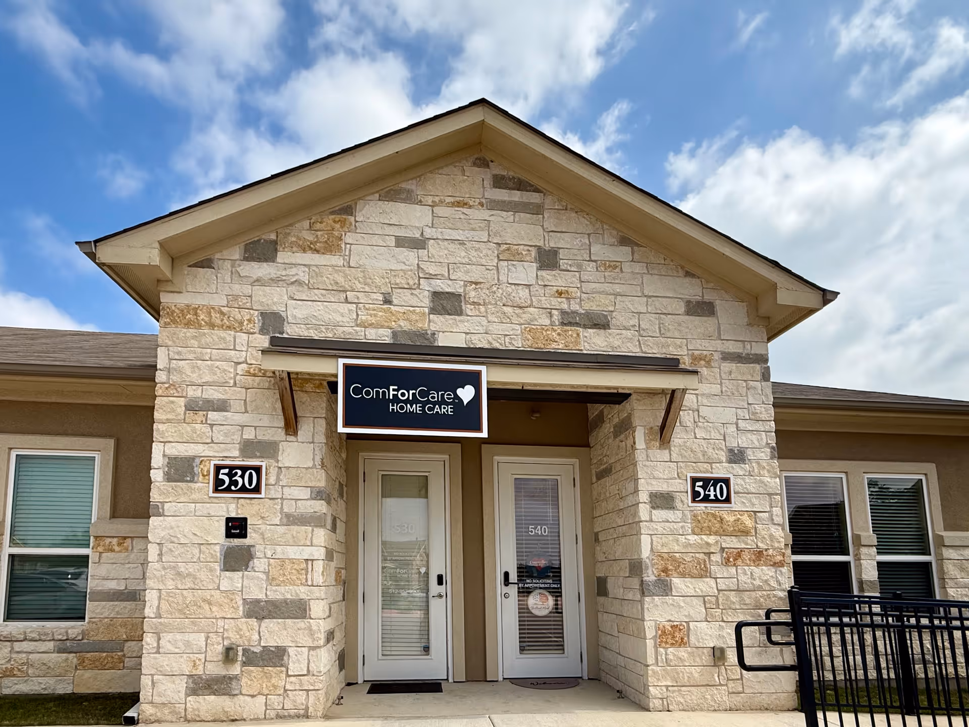 Stone veneer entrance of ComForCare Home Care with two glass doors and plaque numbers.