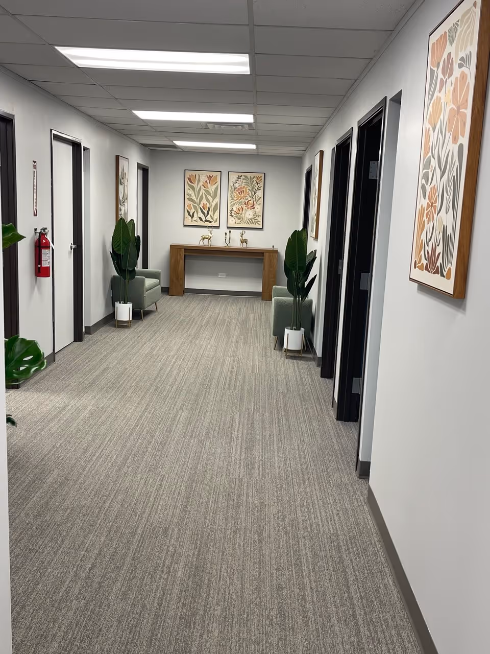 Well-lit hallway in a senior living facility with framed art, plants, and seating.