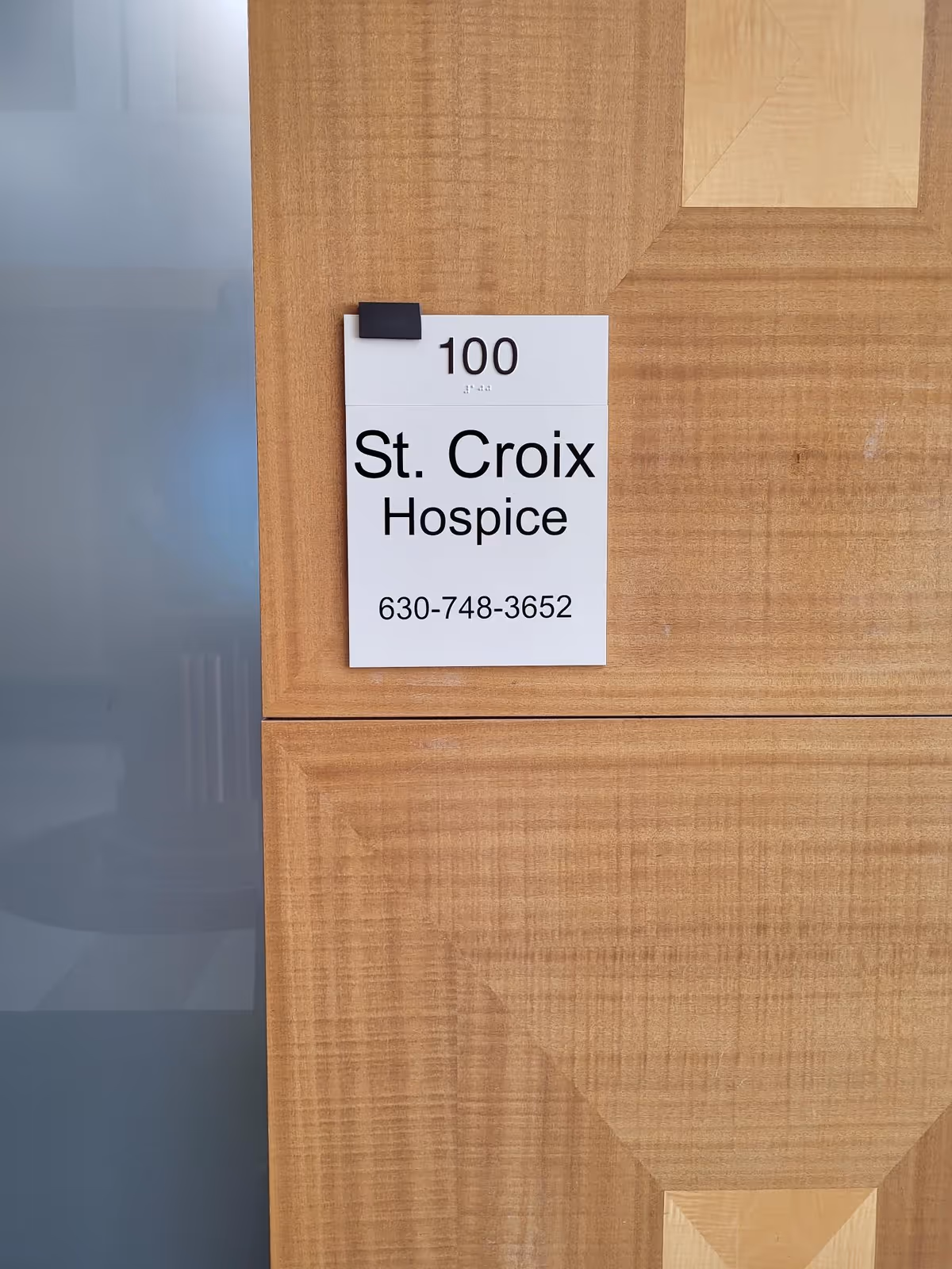 Wooden door with St. Croix Hospice sign and room number 100 in a corridor