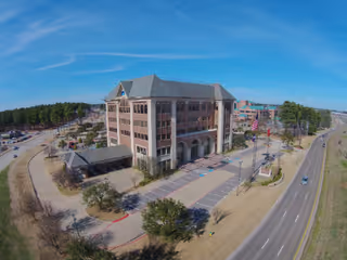 Aerial view of a multi-story brick senior living building with parking and surrounding roads.