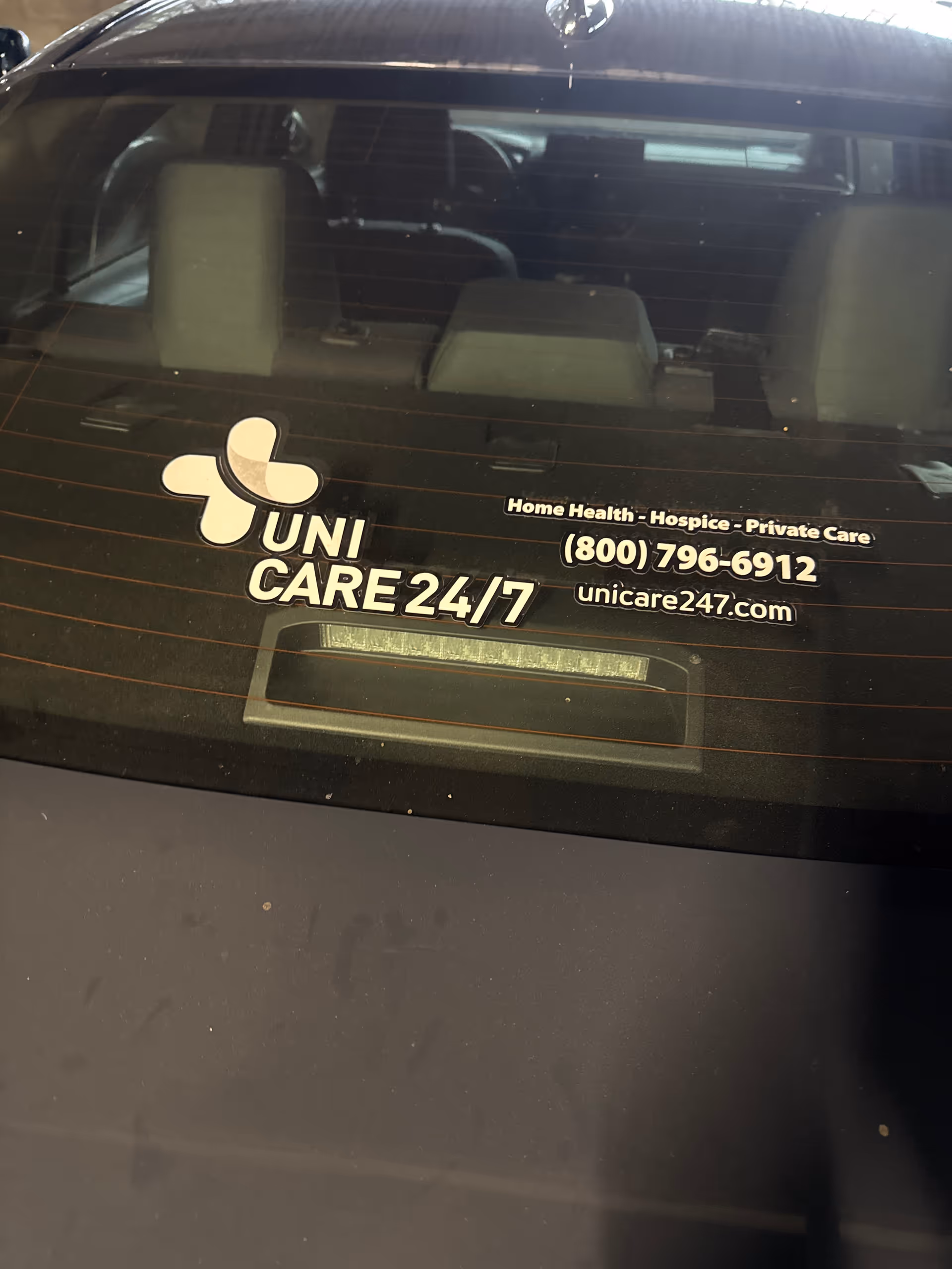 Rear car window displays Uni Care Hospice 24/7 branding and contact information