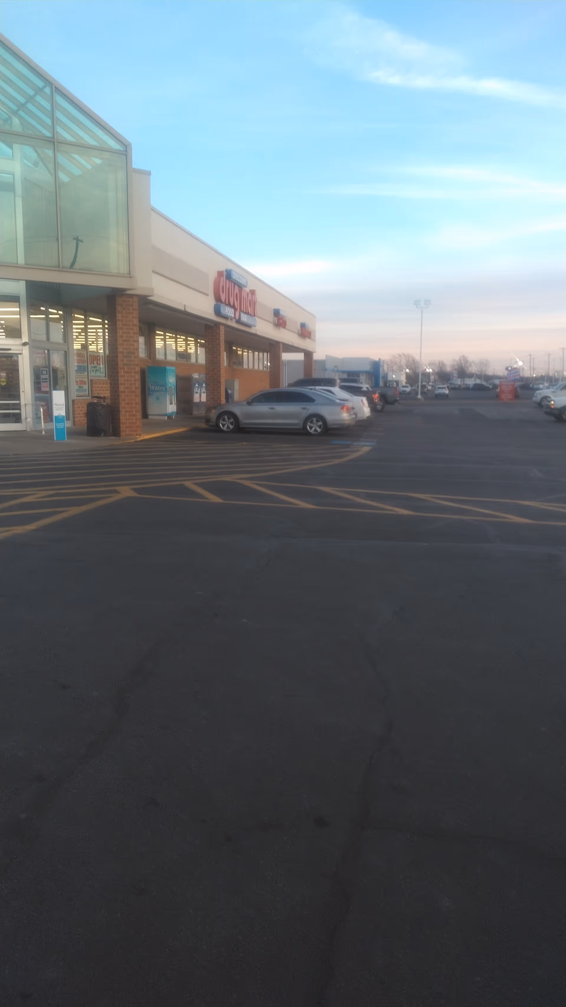 Exterior view of Discount Drug Mart storefront with parked cars and glass entrance.