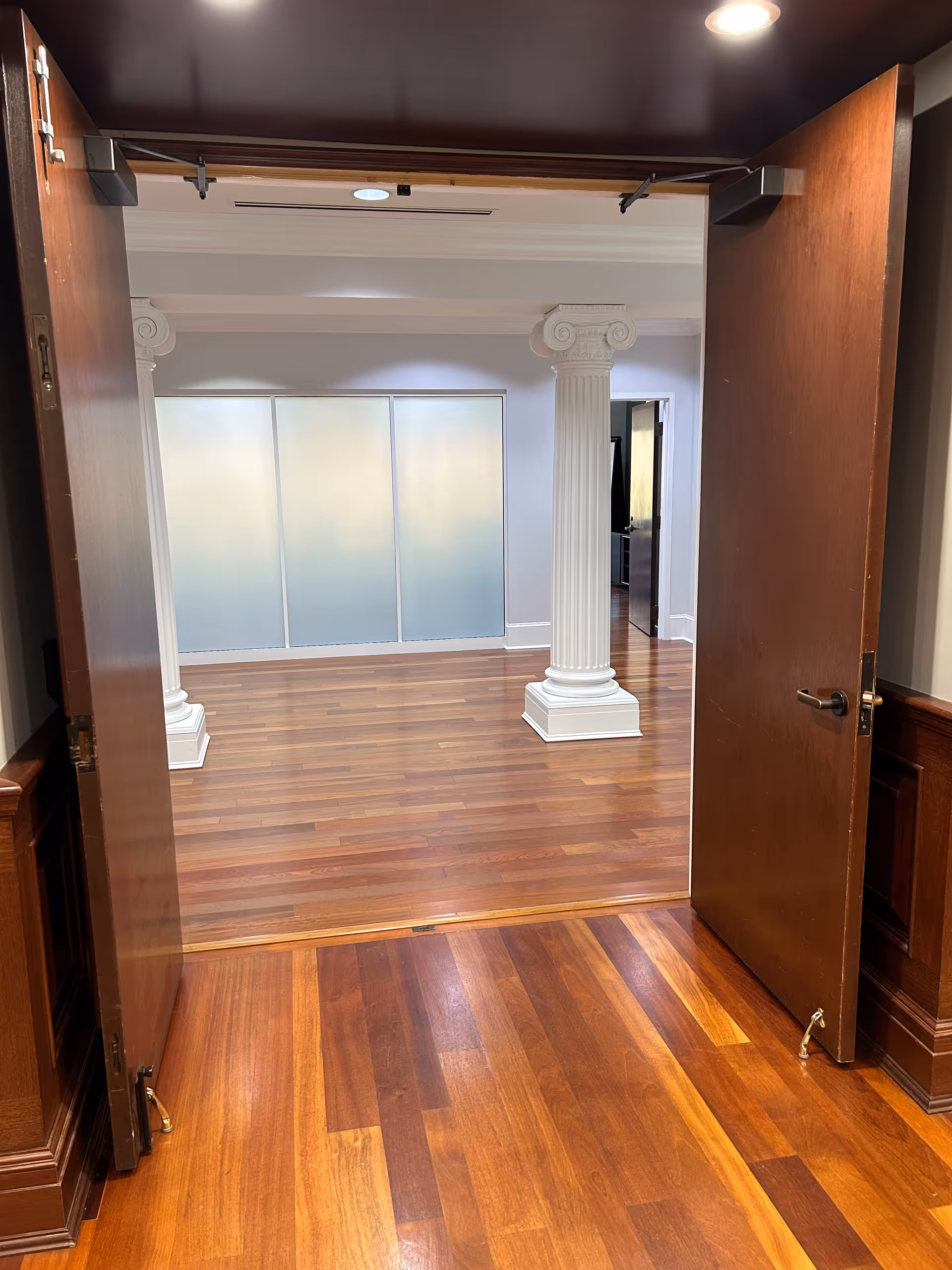 Open double doors reveal a columned interior room with wooden flooring.