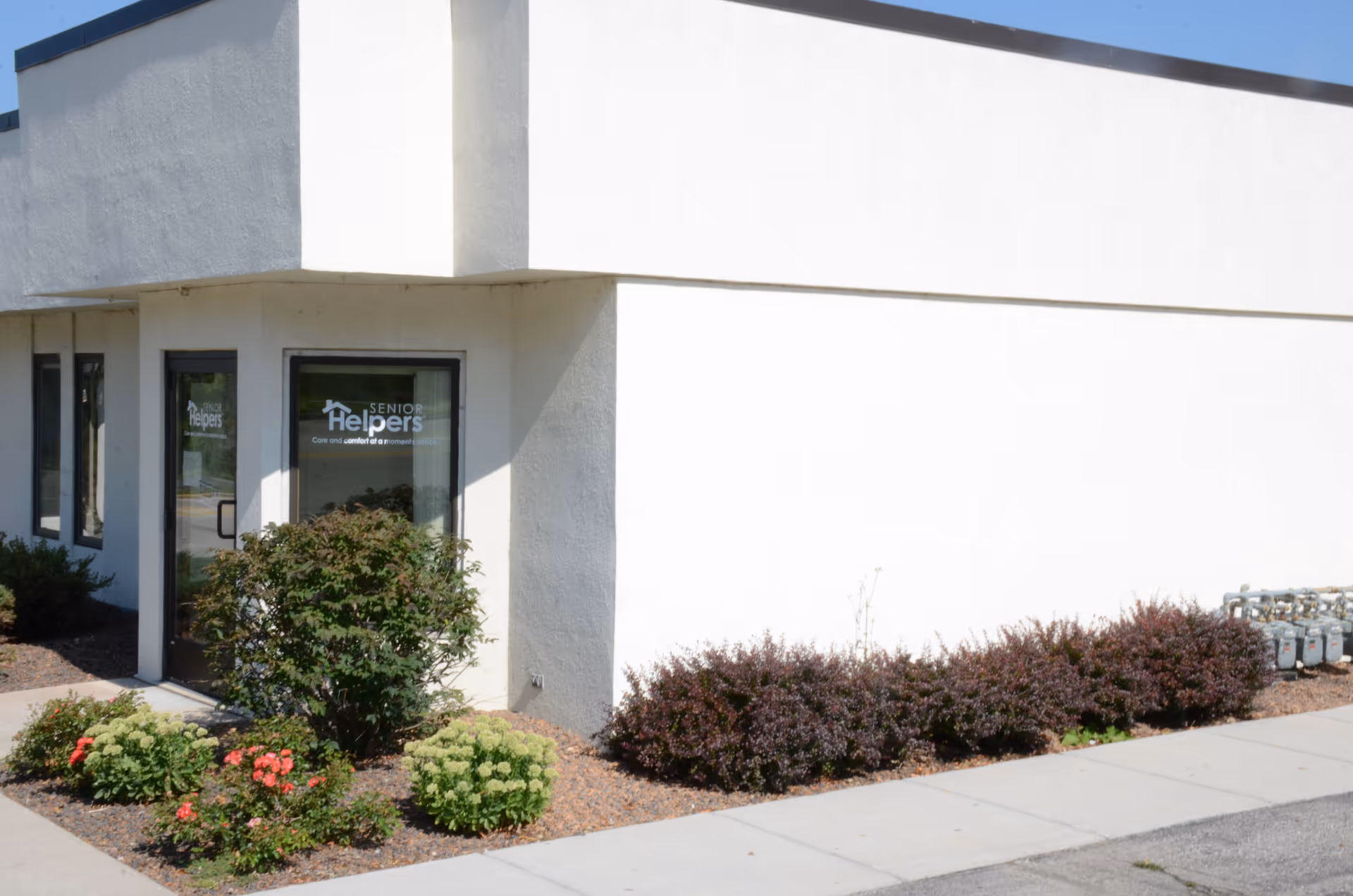 White building entrance labeled Senior Helpers with glass doors, surrounded by desert landscaping and sidewalk.