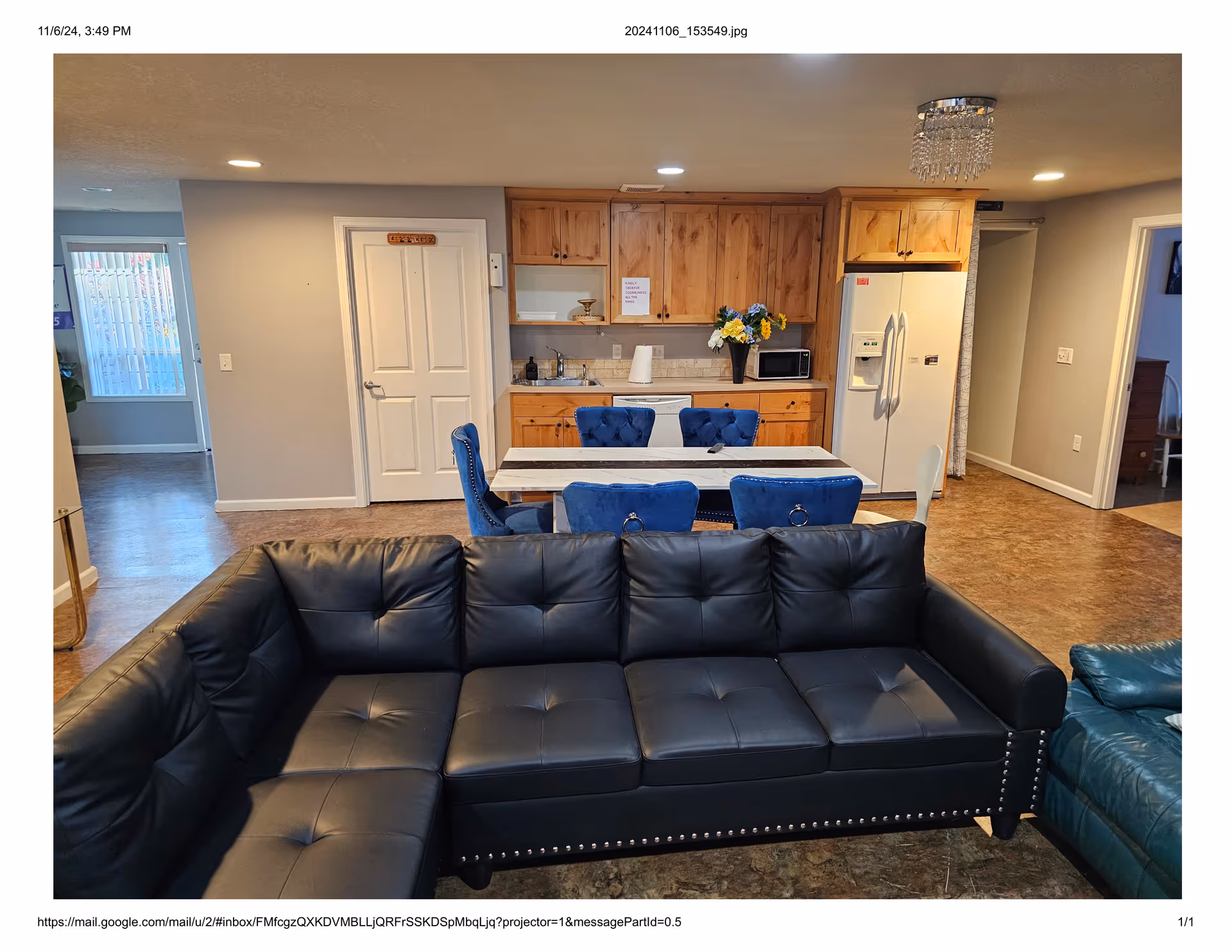 Interior living area with a black leather sectional, blue chairs, and a kitchen in the background.