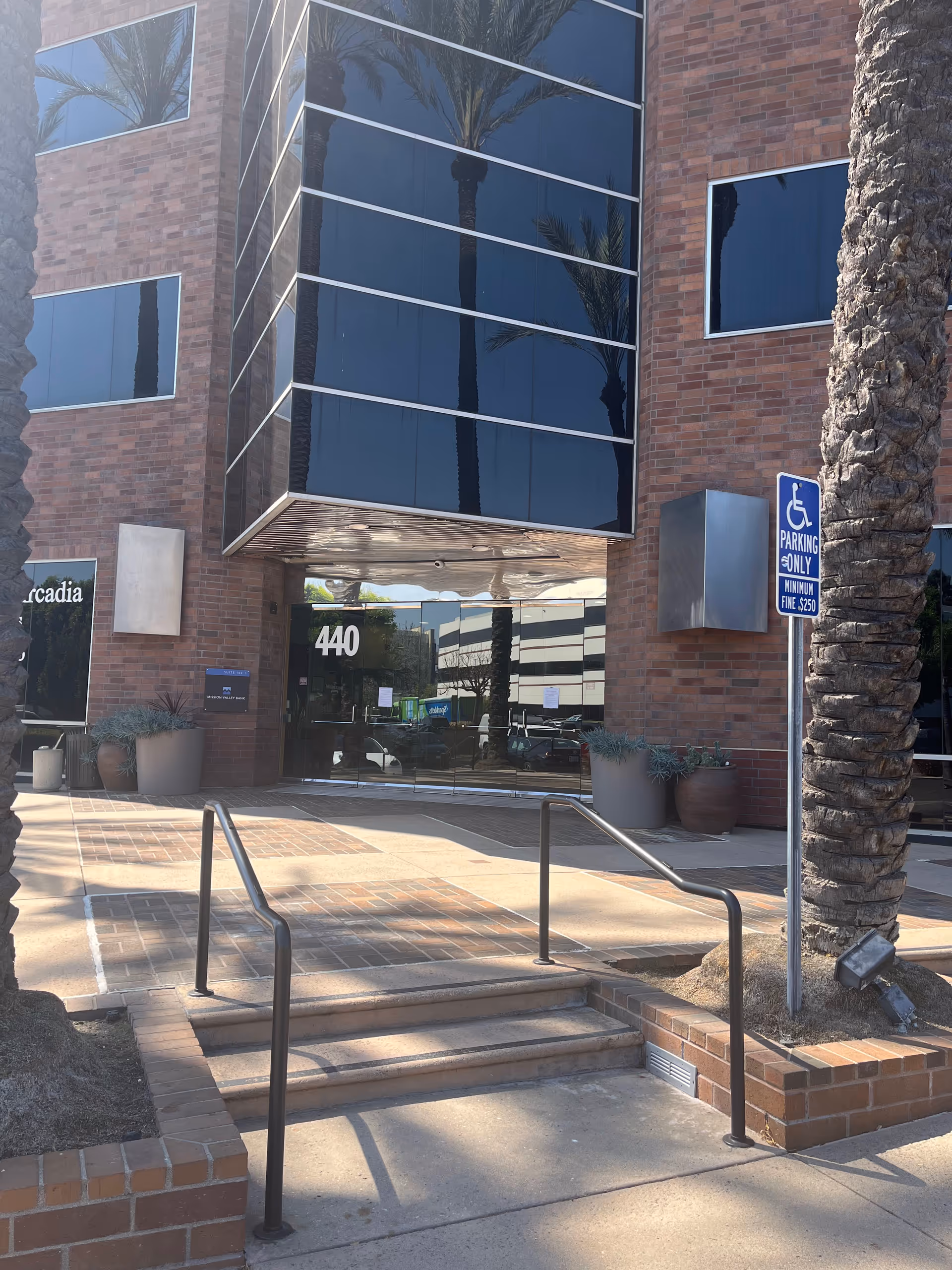 Exterior view of a brick building entrance with glass windows and a handicap parking sign.