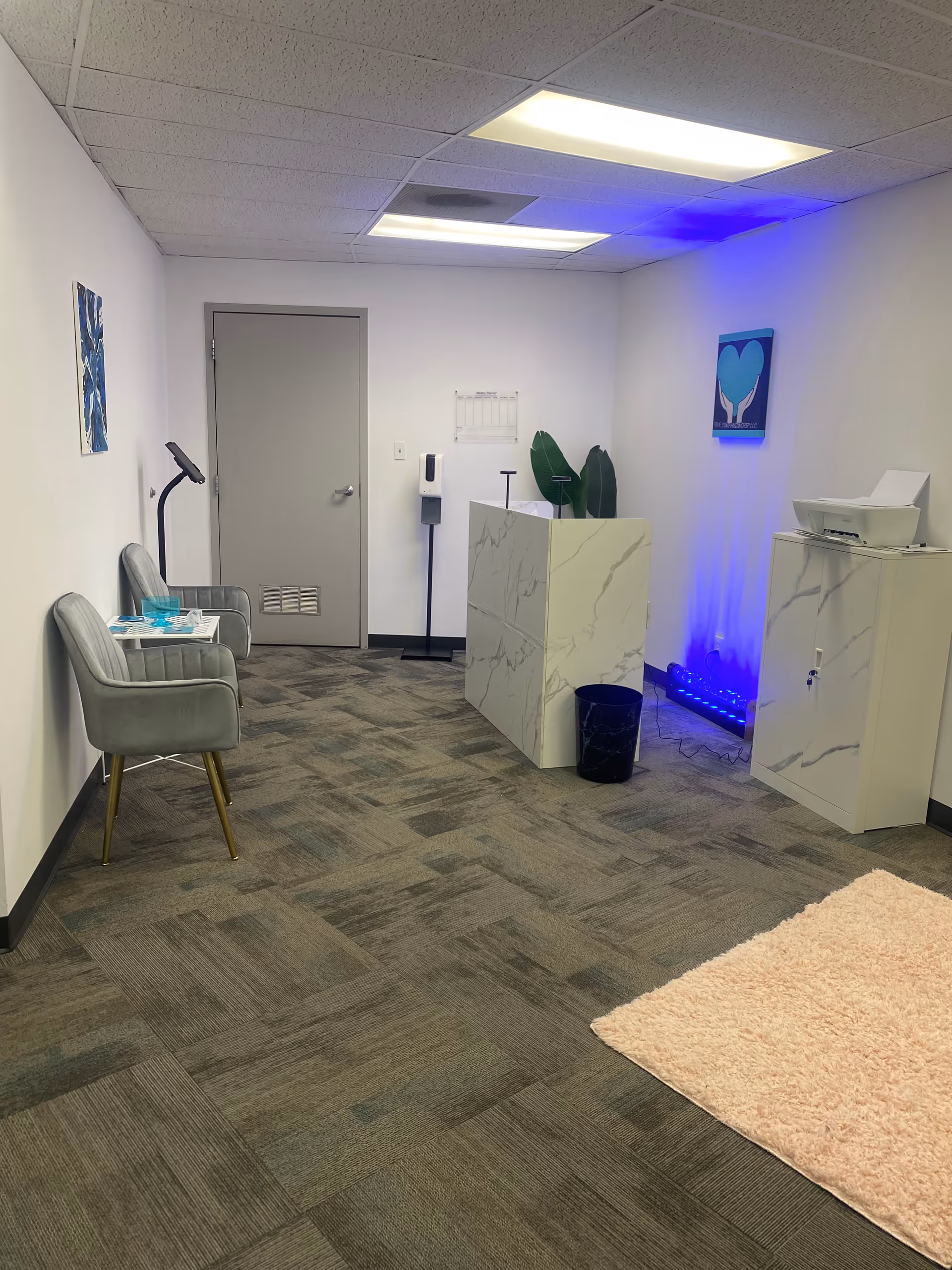 Lobby area with marble reception desk, blue accent lighting, and two gray chairs.