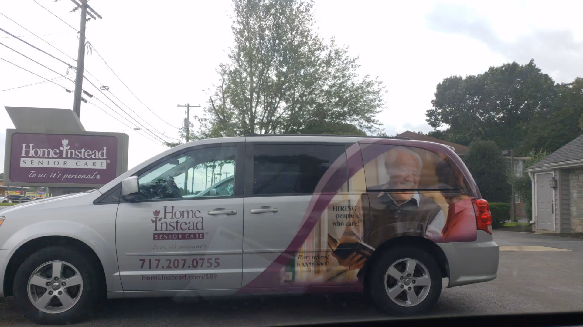 Branded Home Instead Senior Care van parked outside the facility beside a matching sign.