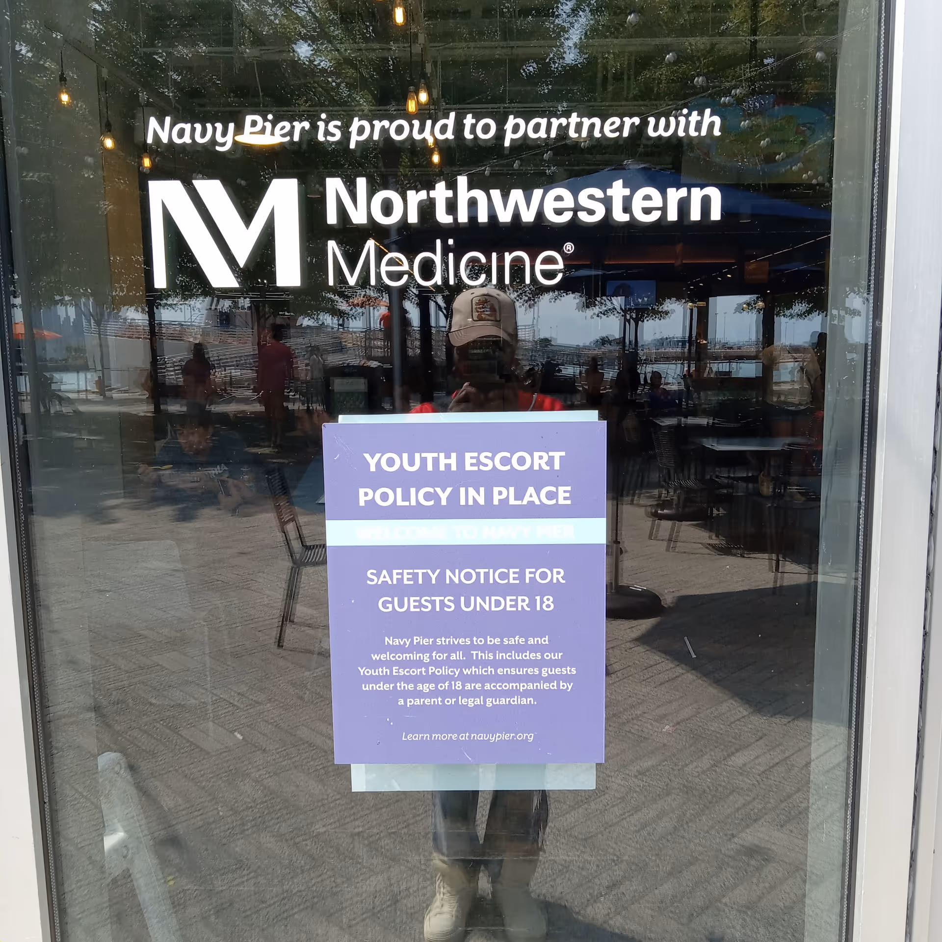 Glass storefront shows Navy Pier along with Northwestern Medicine logo and purple Youth Escort Policy sign.