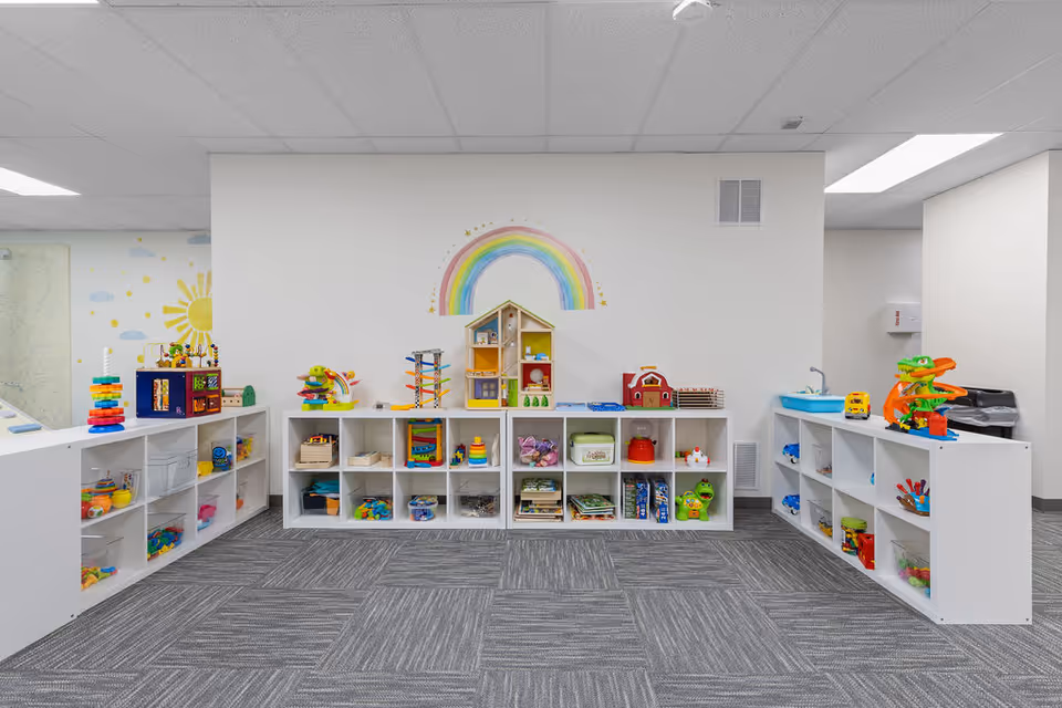 Bright children's playroom with white cubbies, colorful toys, and a rainbow wall mural.