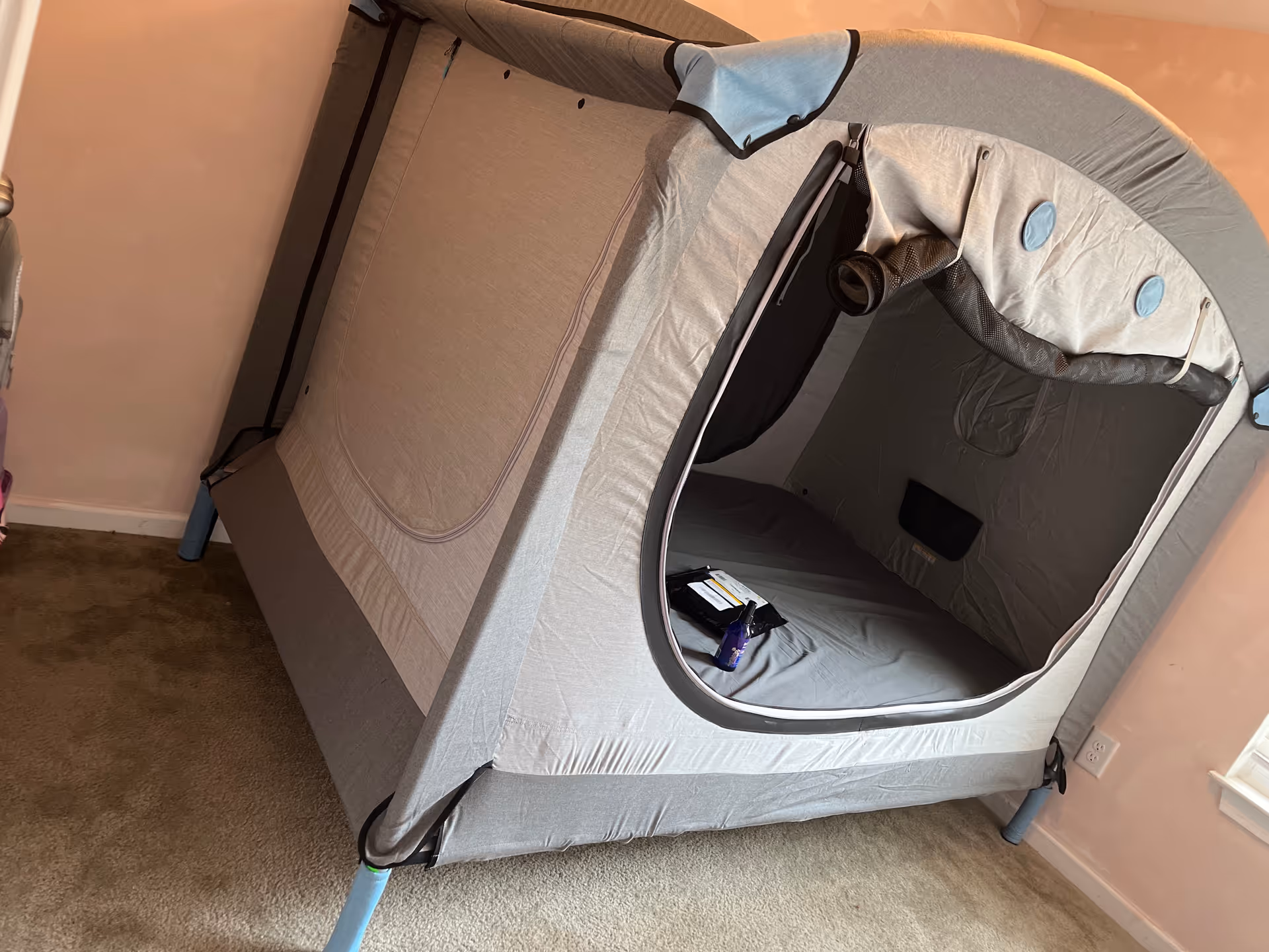 Gray pop-up privacy tent set up in a pink-carpeted room.