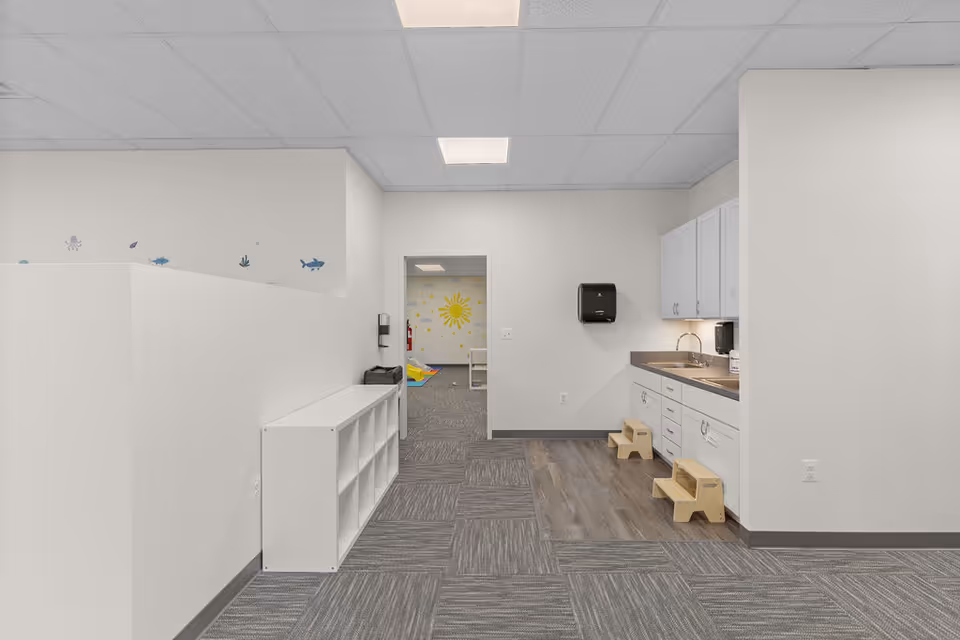 Bright interior kitchenette with sink, white cabinets, and cubbies in a senior facility.
