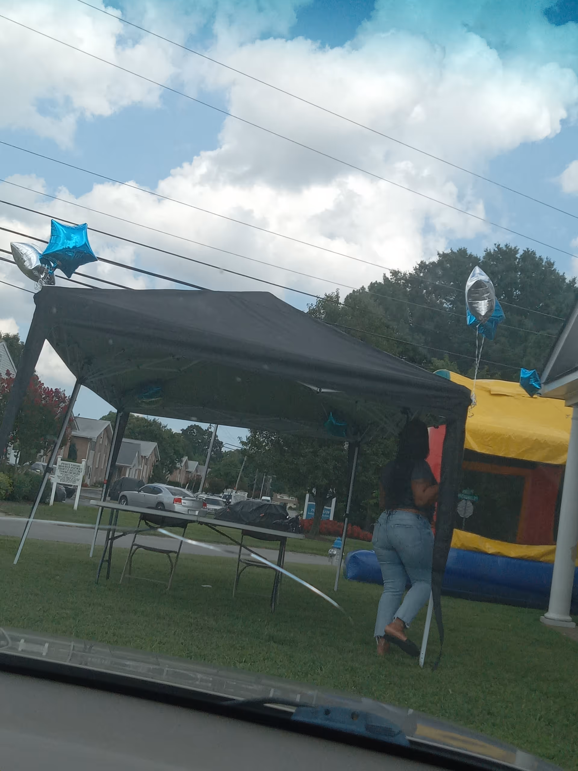 Outdoor event with a black canopy tent, balloons, tables, chairs, and a person nearby.