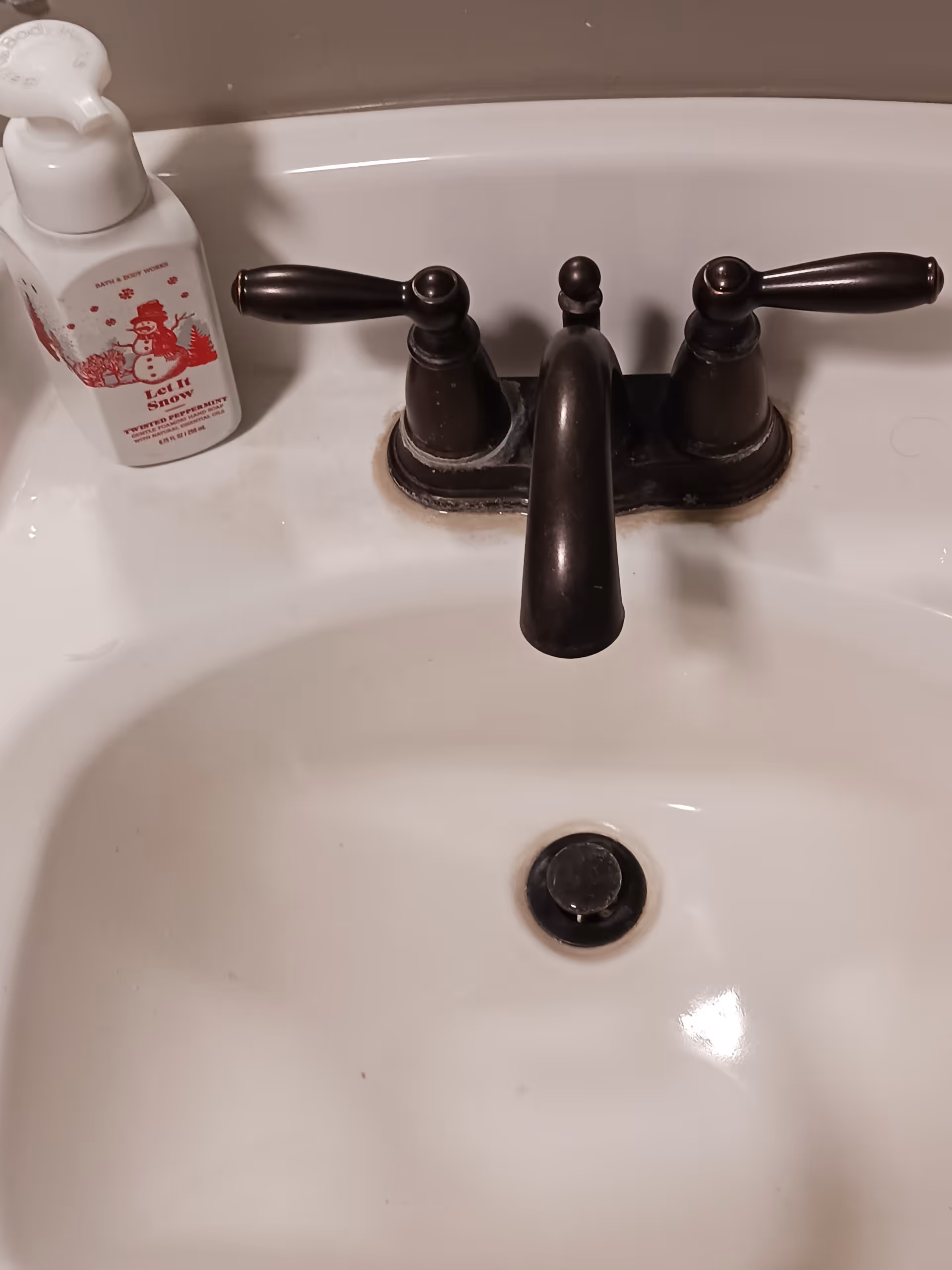 A white bathroom sink with a dark faucet and holiday soap bottle.