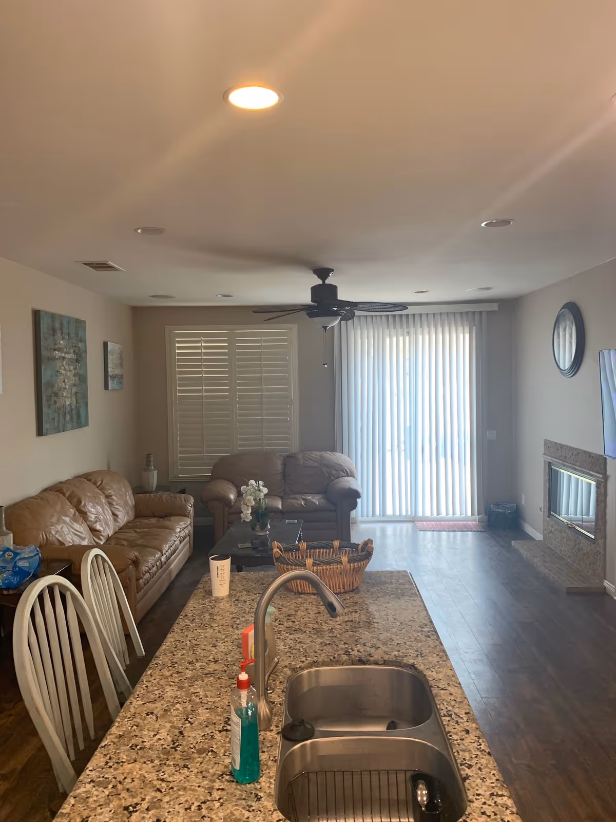 Open-concept living area with leather sofas, granite island, and sliding door blinds.