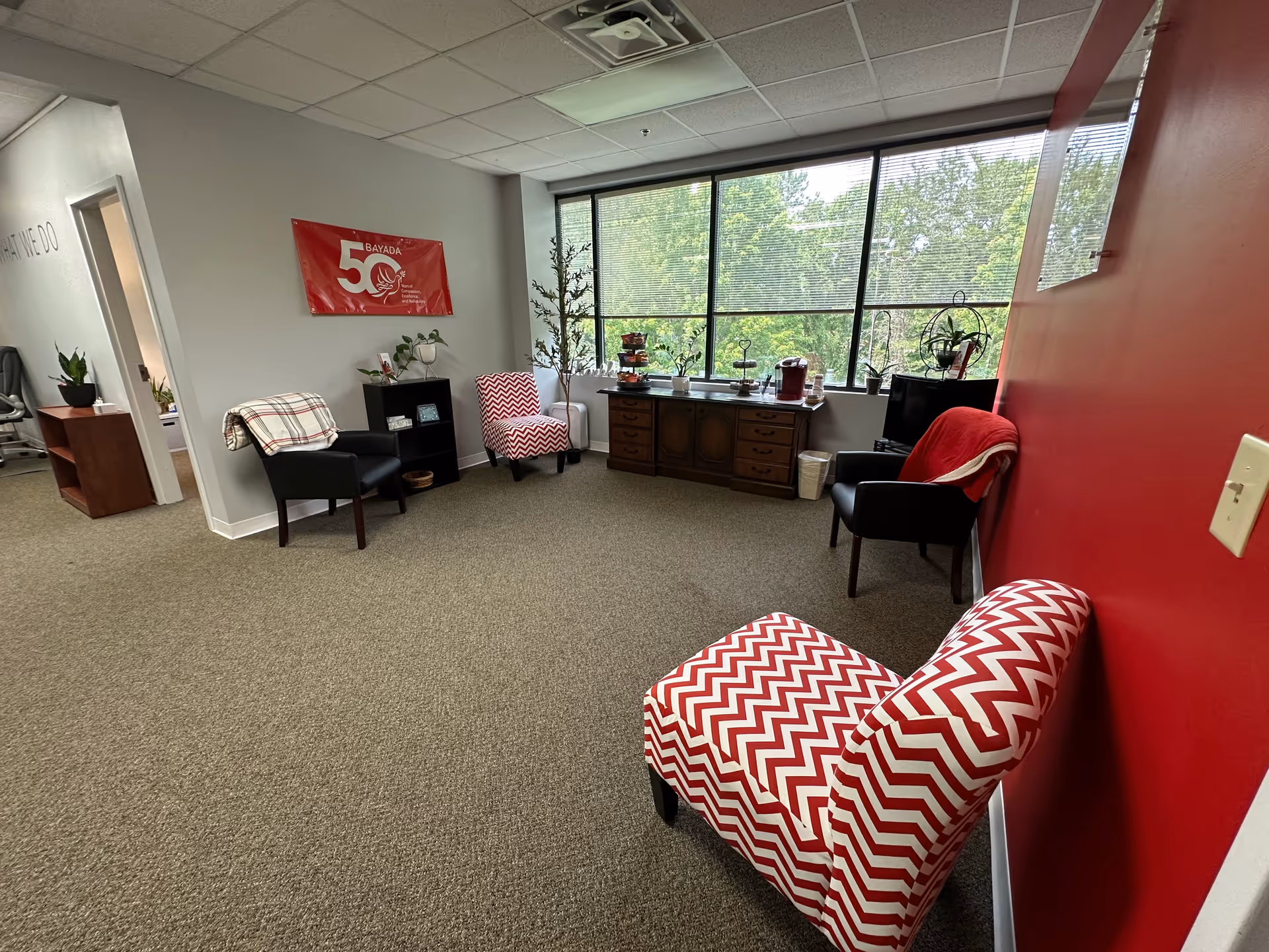 Bright BAYADA Assistive Care lounge with red accent wall, chairs, and a large window.