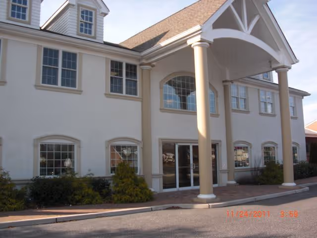 Exterior view of a beige two-story Visiting Angels senior home with a covered entrance and columns.