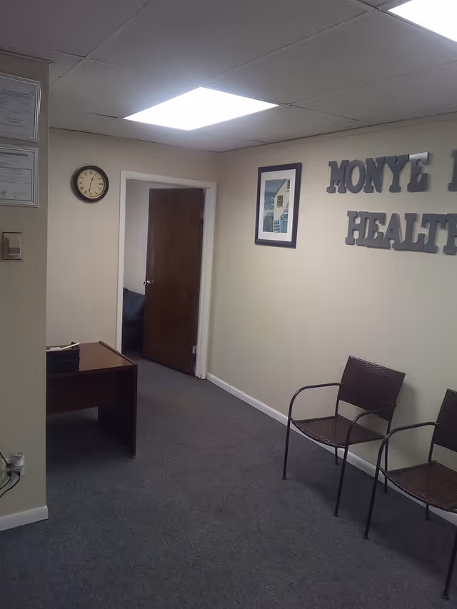 Interior reception area with desk, chairs, clock, and a Monye Health sign on the wall.