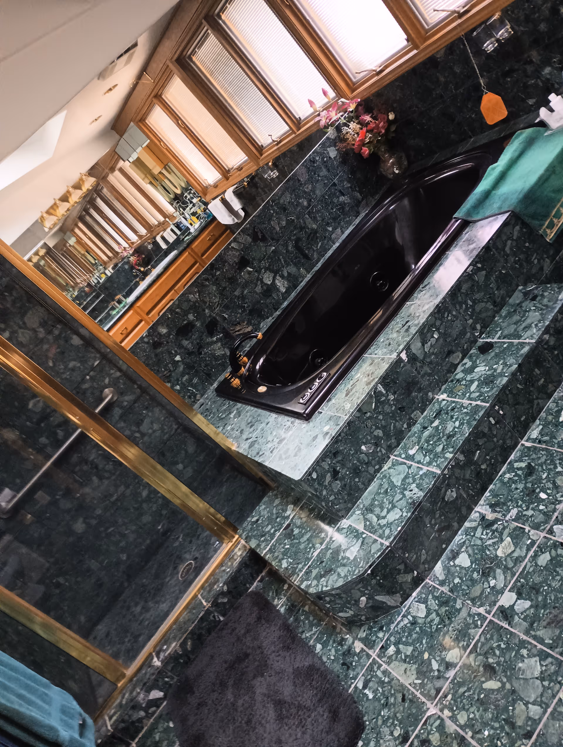 Green marble bathroom with a black soaking tub and mirrored cabinets.