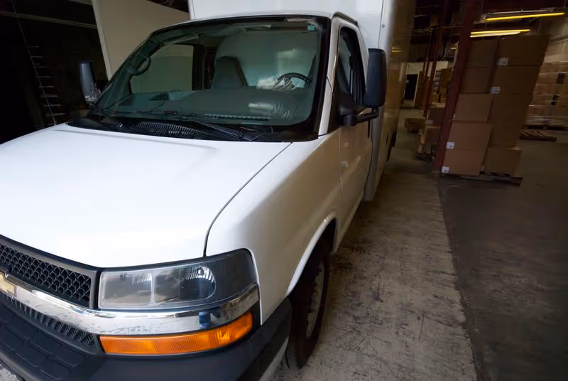 White delivery van parked inside a warehouse loading dock with stacked boxes in background.