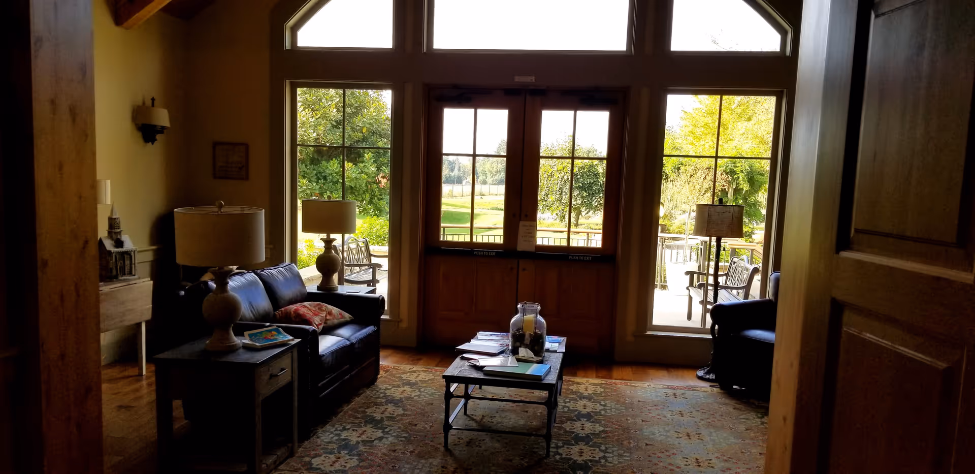 Cozy living room with sofa, lamps, coffee table, rug, and windows opening to an outdoor patio.