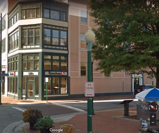 Street corner storefront building with Bonchon restaurant, a lamppost, crosswalk, and trees.