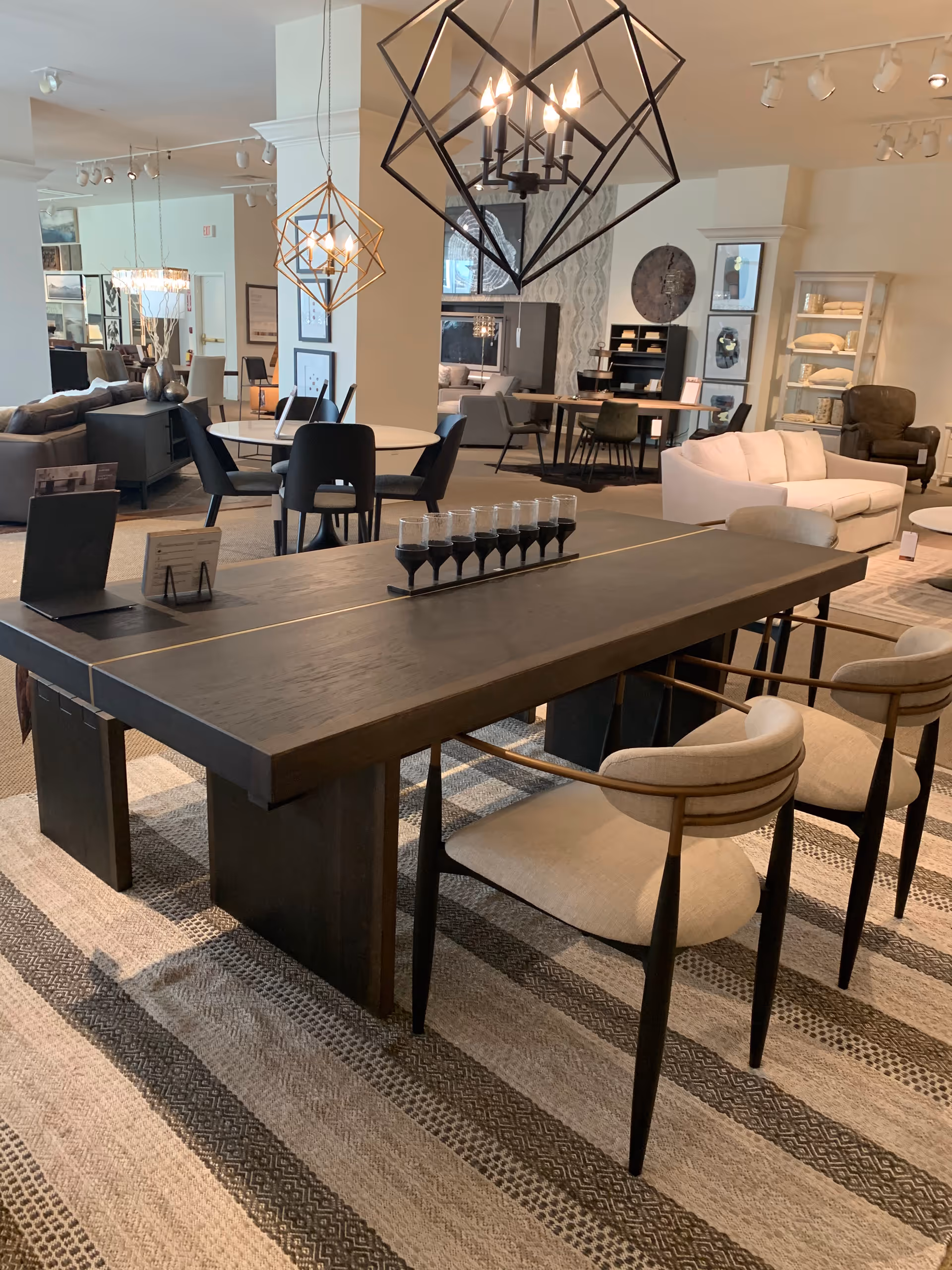 A modern senior living showroom with dark wood dining table, chairs, and pendant lights.