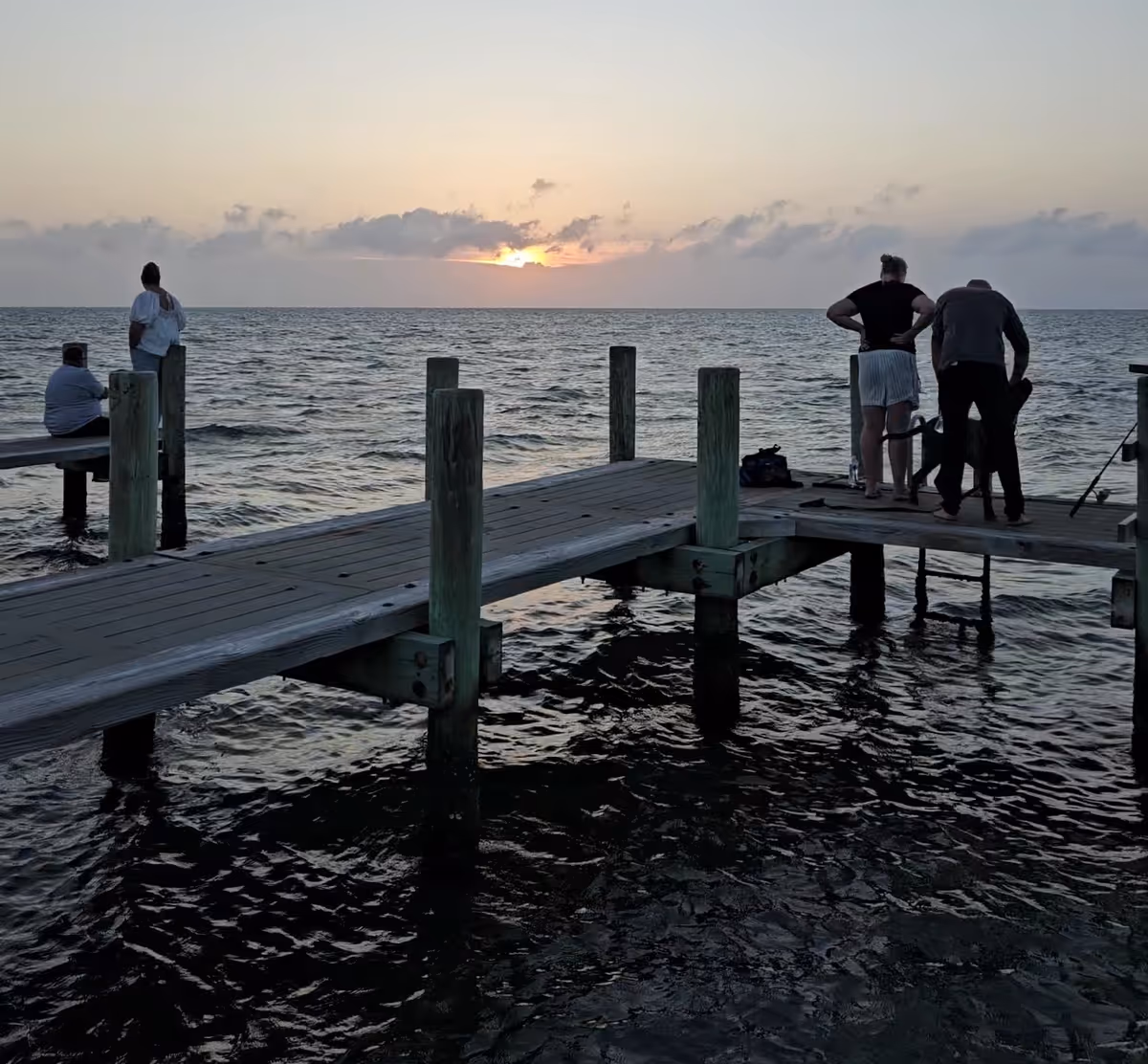 Sunset over the ocean with a wooden pier and several people standing on it.