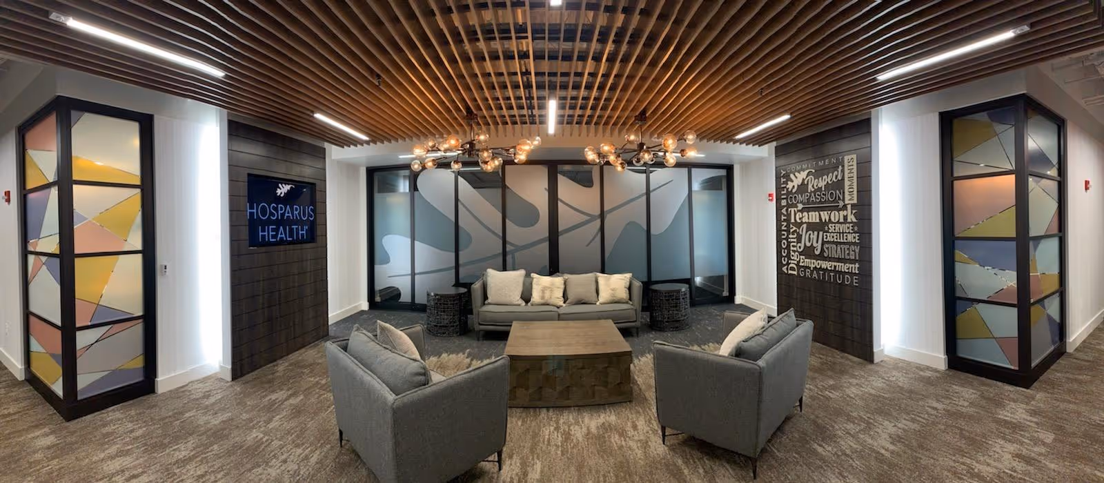 Contemporary Hosparus Health lobby lounge with couches, a central coffee table, and decorative wall panels.